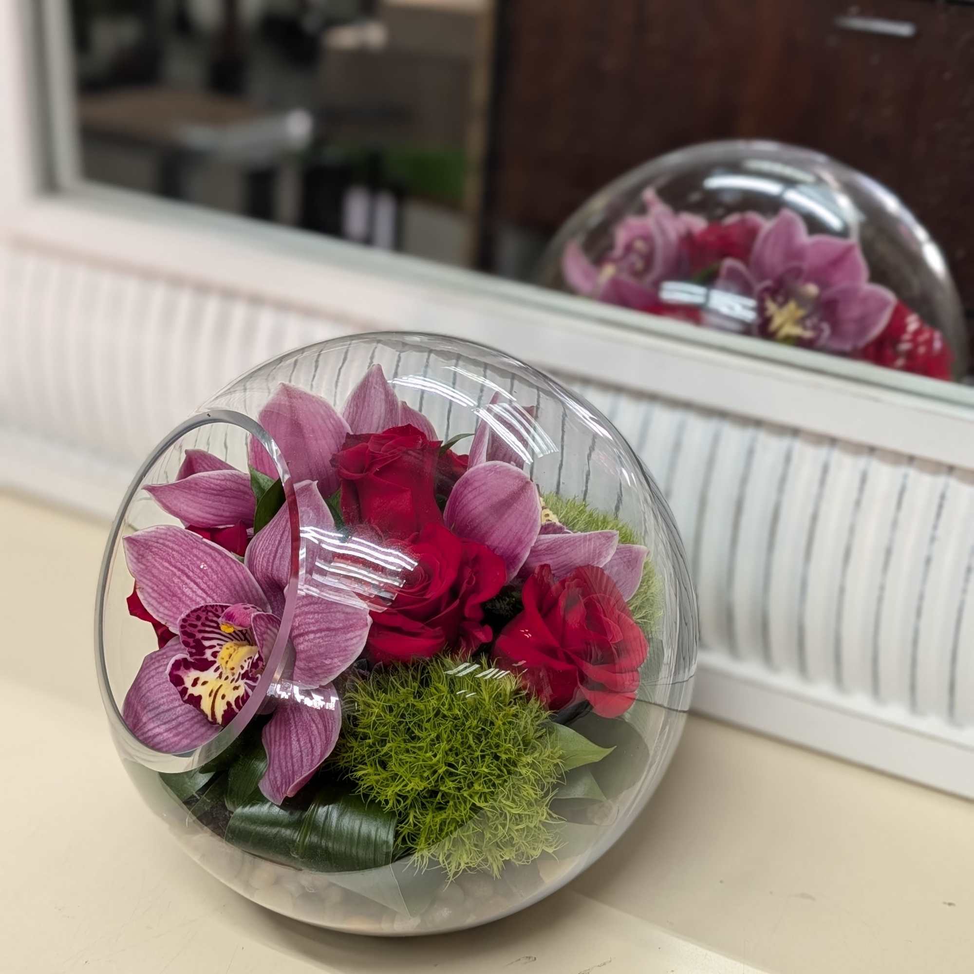 Pink and red floral arrangement in a clear round dome box