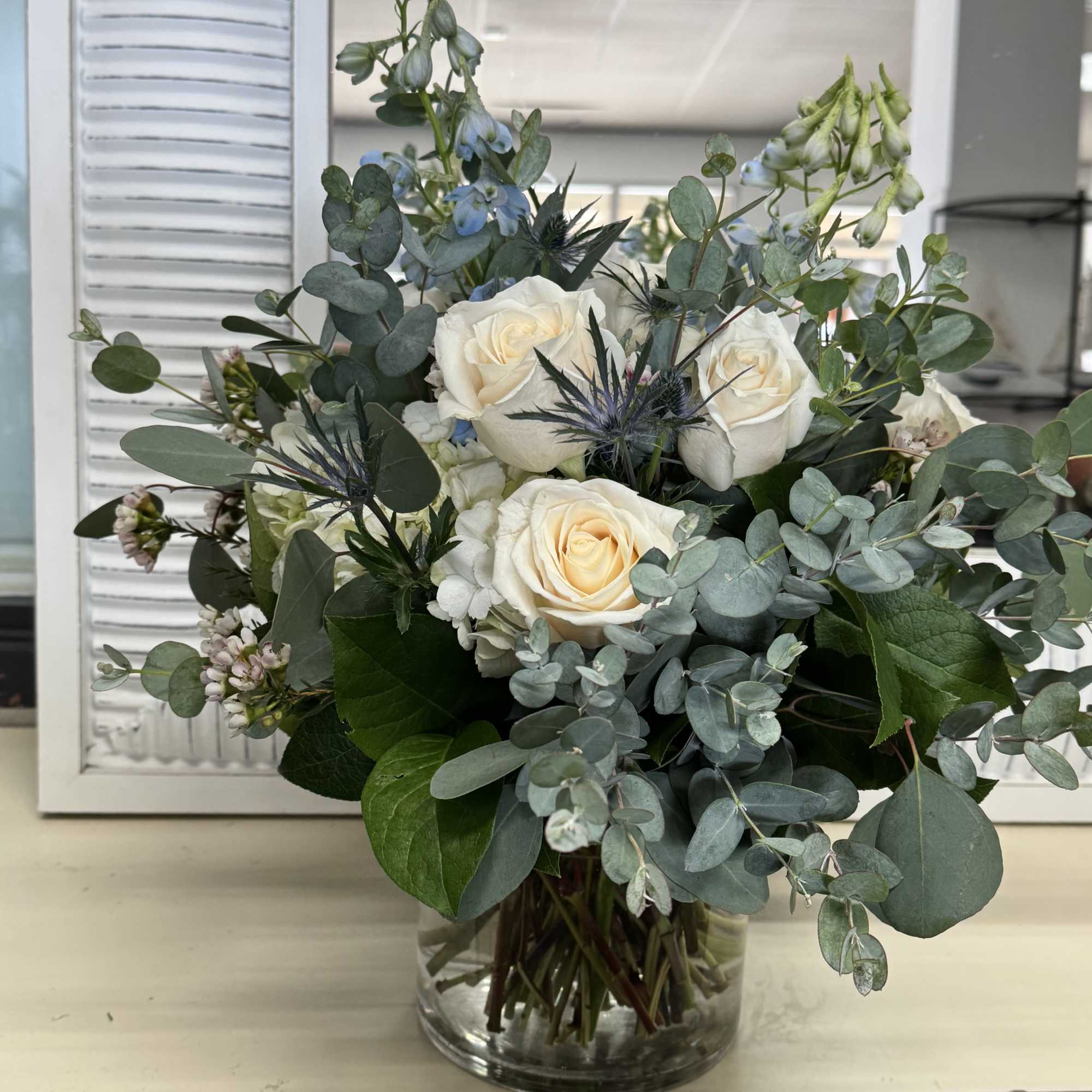 White roses and blue flowers in a glass vase with eucalyptus