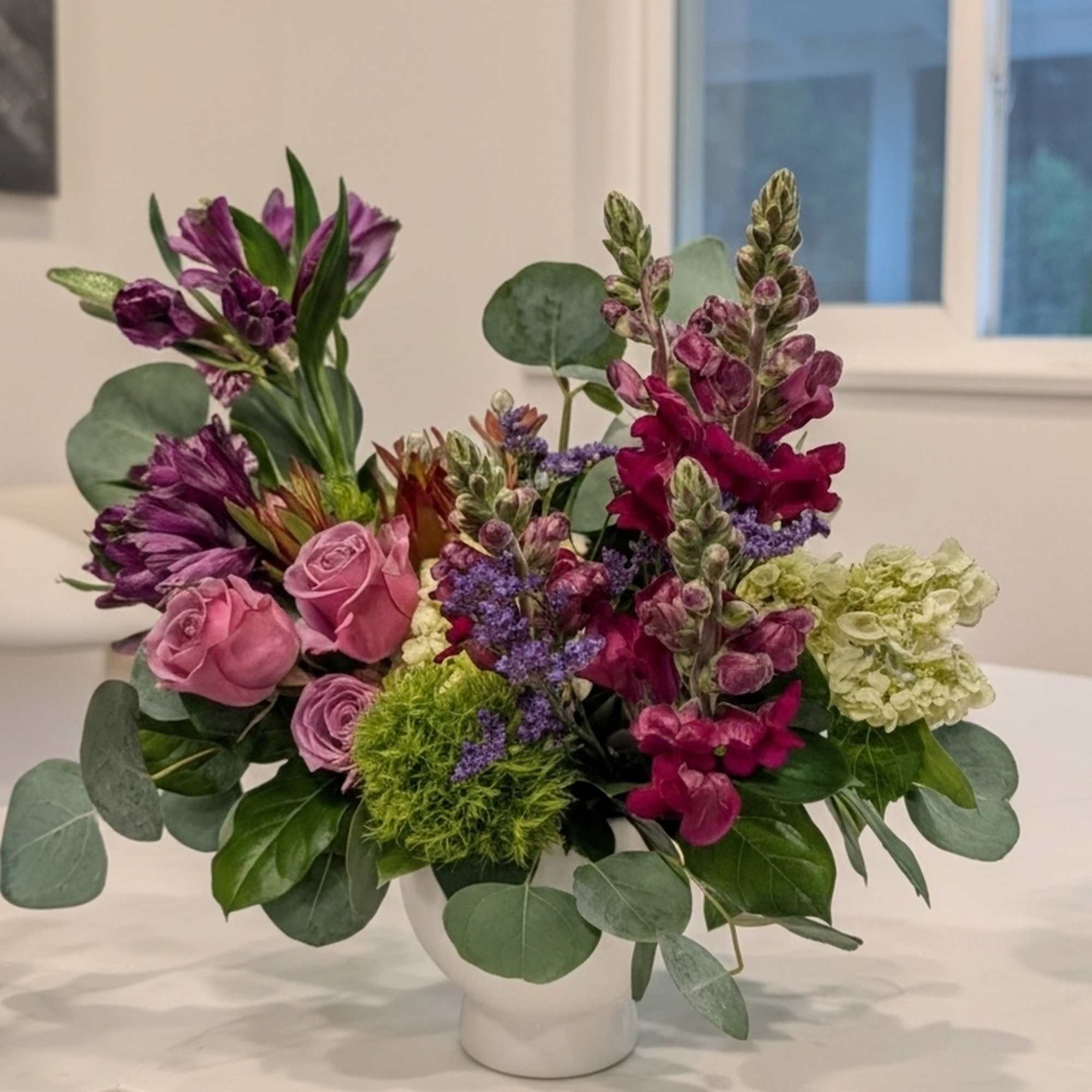 Mixed bouquet of pink and purple flowers in a white vase
