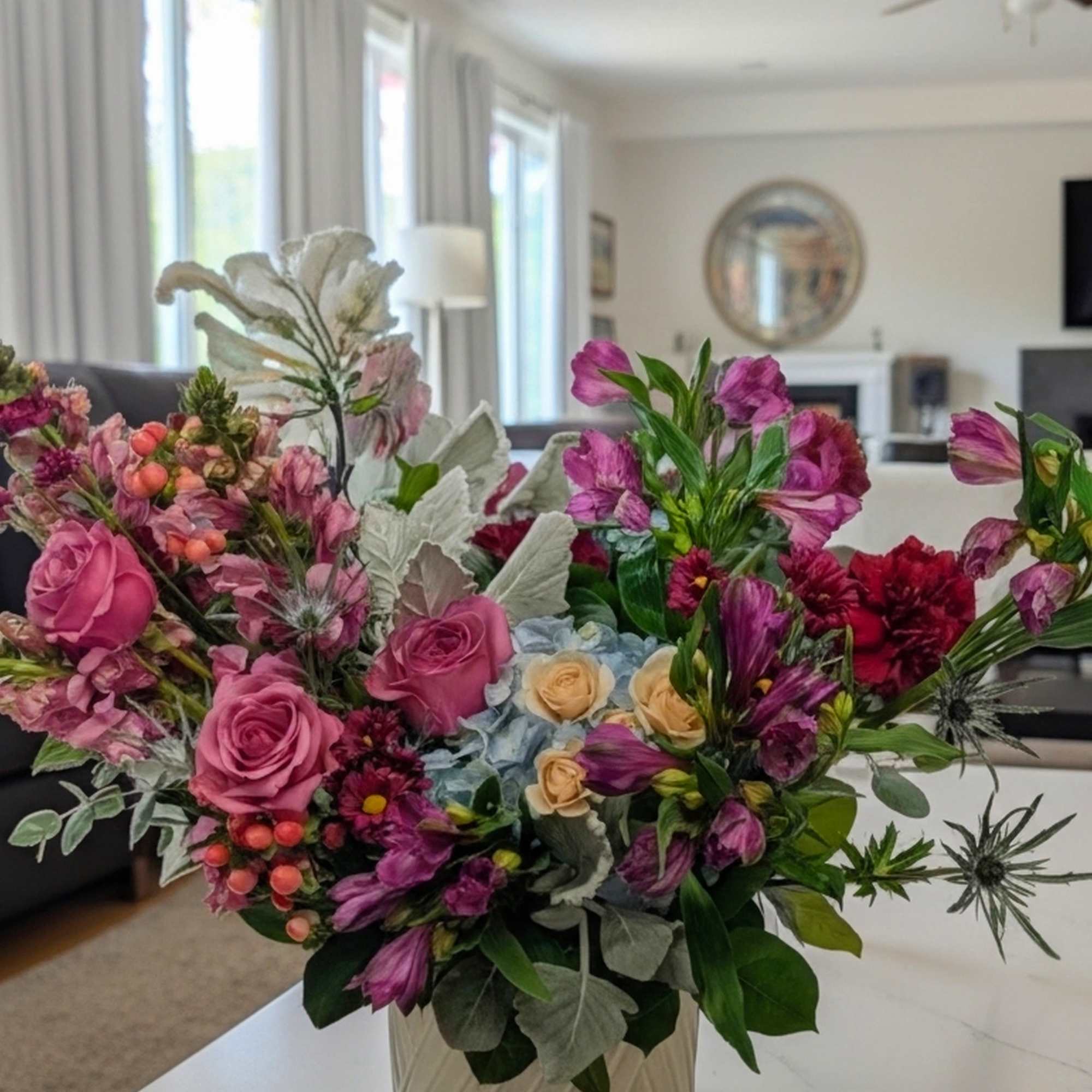 Mixed bouquet of pink and purple flowers in a cream vase