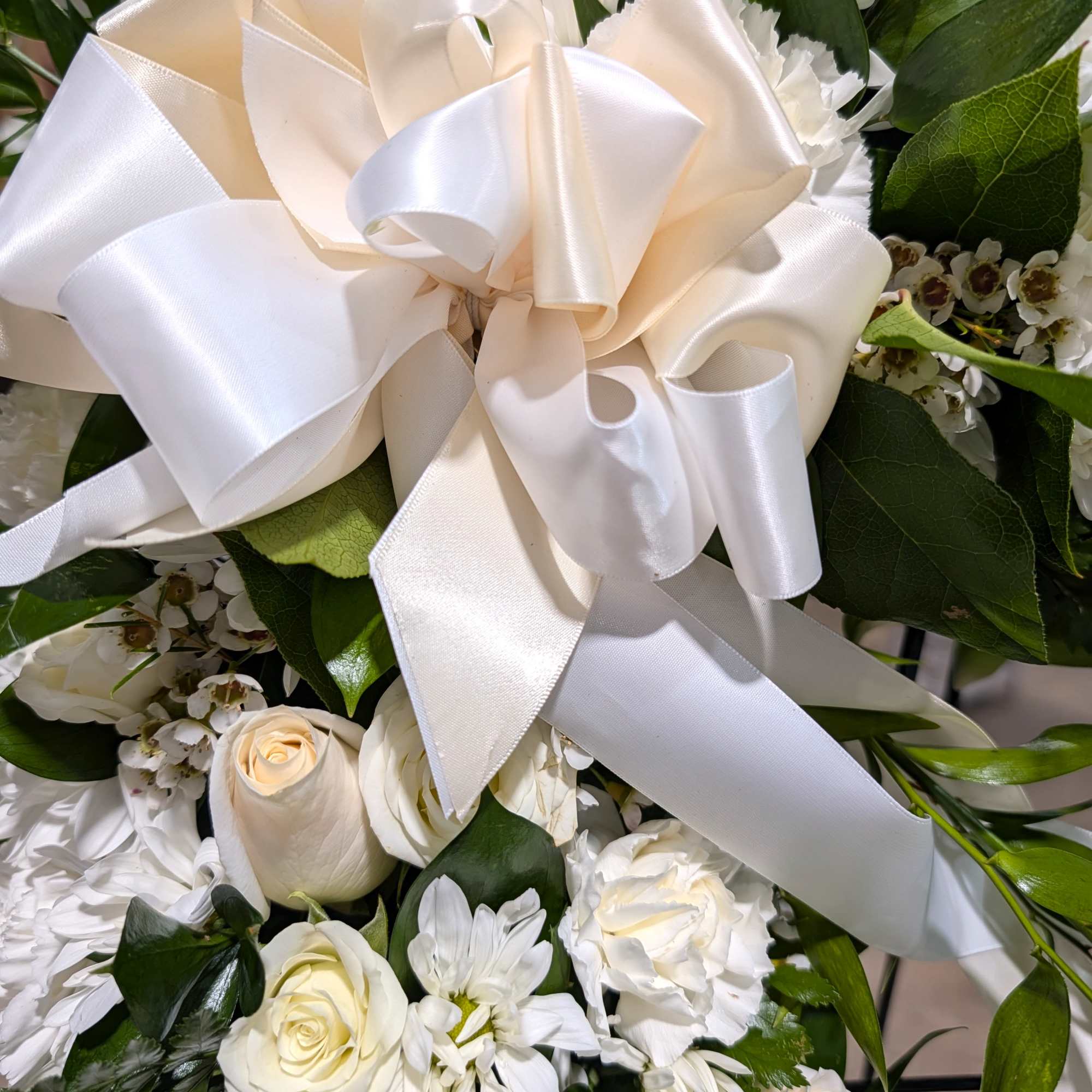 18" open heart decorated with white seasonal flowers accent with a bow.
