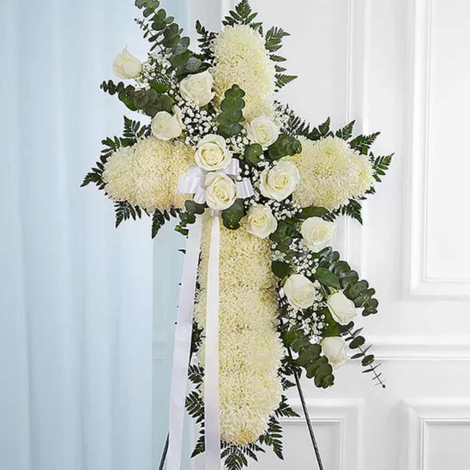 White floral cross on an easel with ribbon and greenery