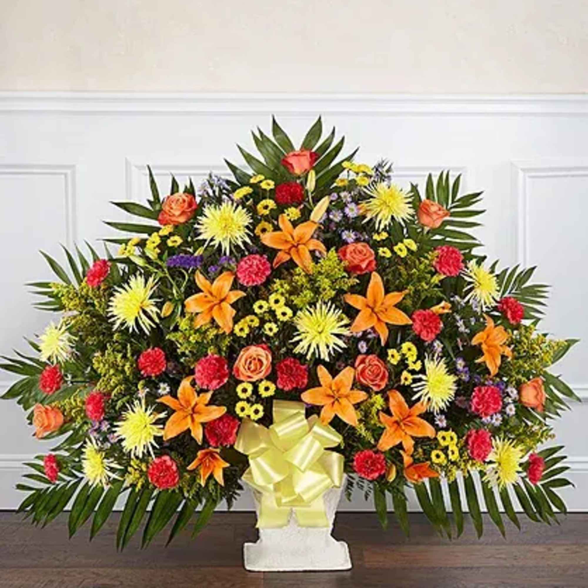 Large colorful floral spray in a white pedestal vase with a yellow bow