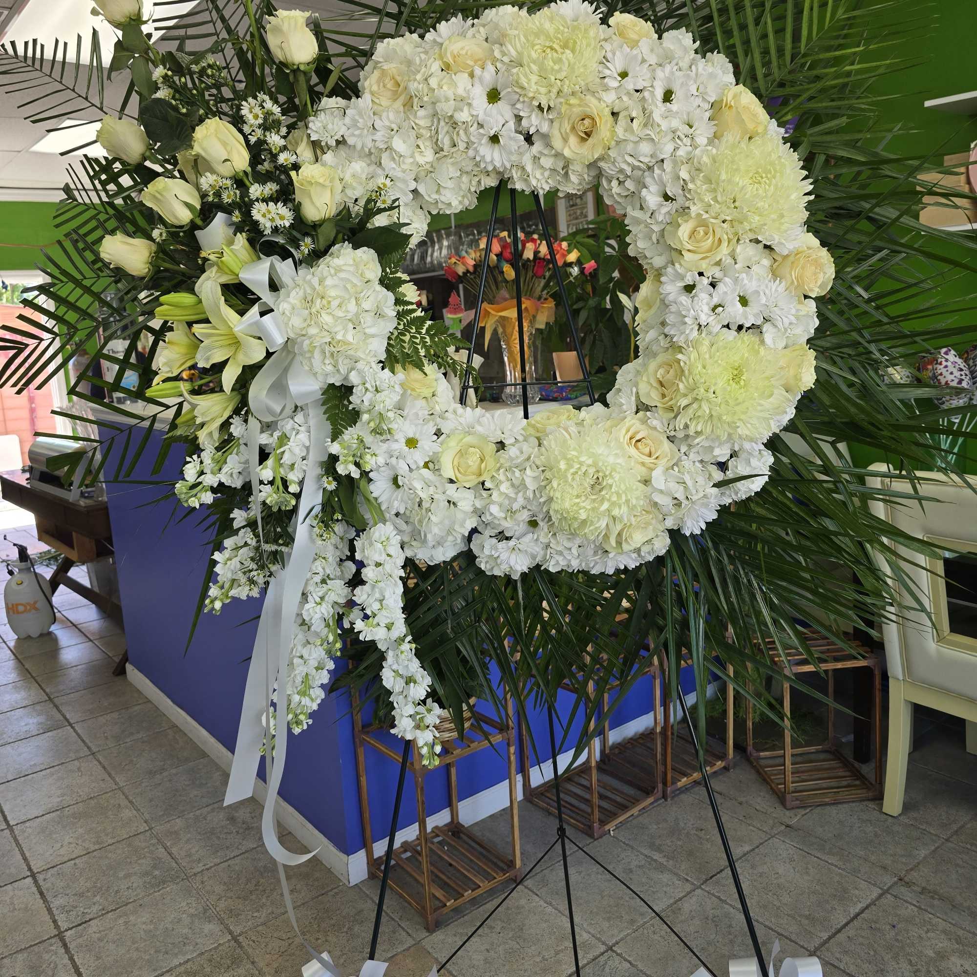 Large white floral wreath on a stand with ribbon bows