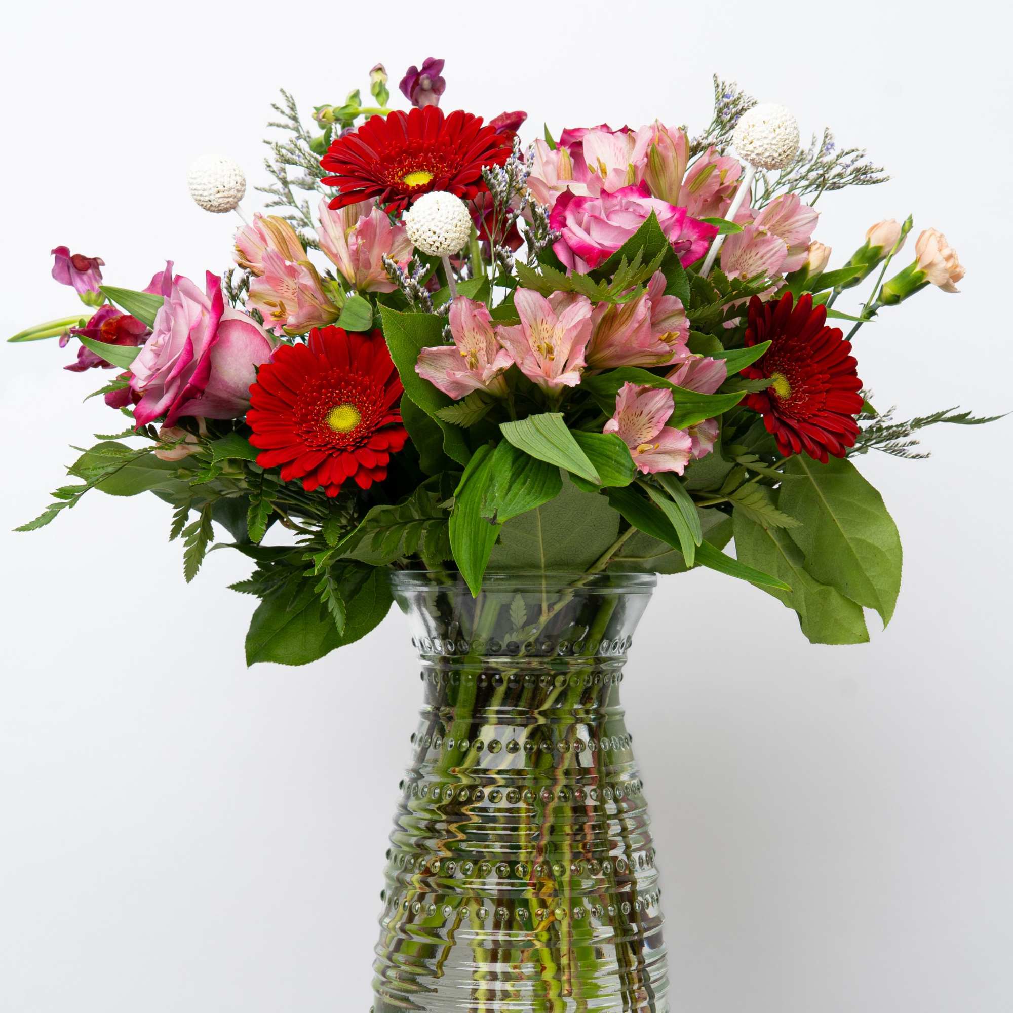 Bouquet of red gerbera daisies and pink flowers in a glass vase