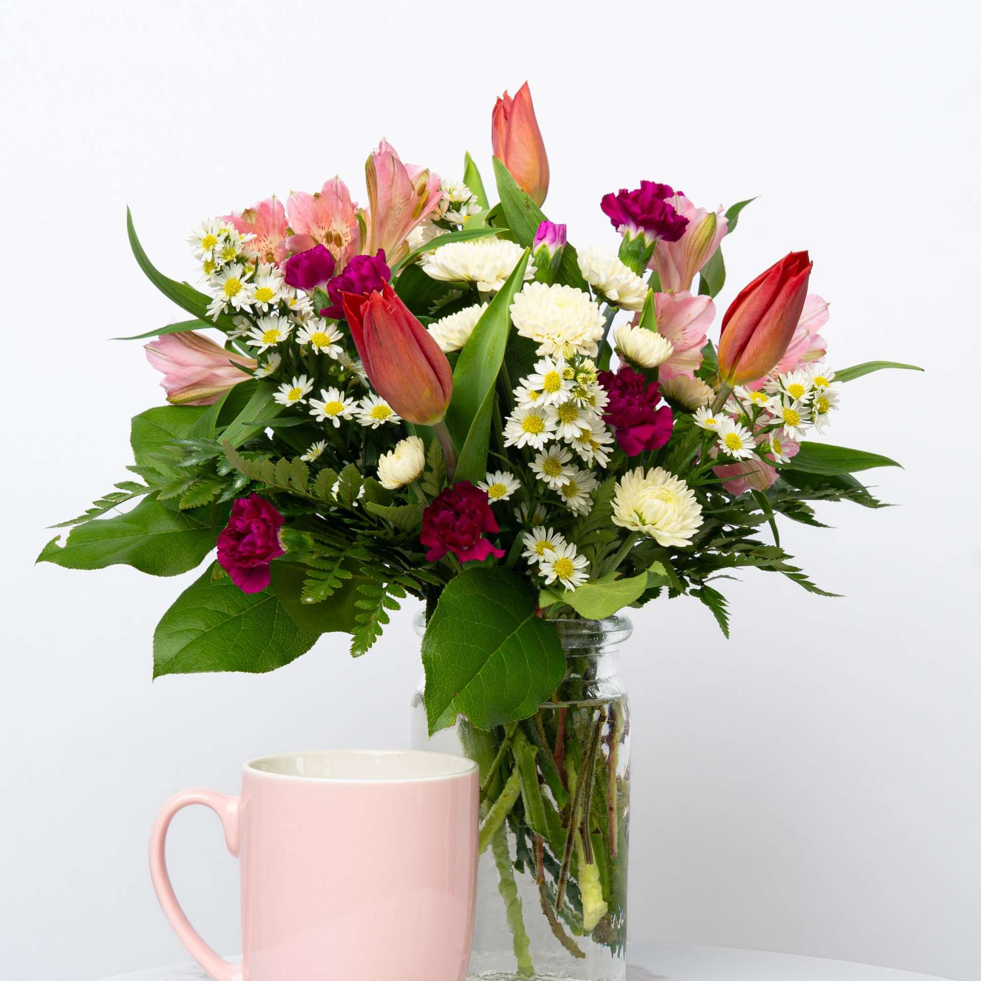 Mixed bouquet in a glass vase with a pink mug in front