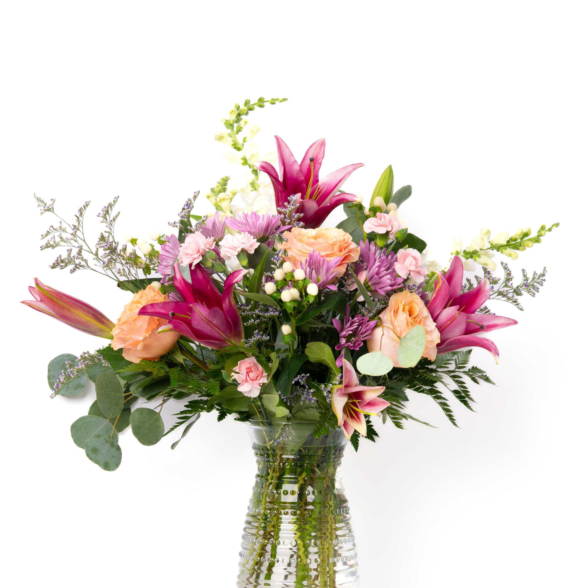 Mixed bouquet of pink lilies, peach roses, and pastel blooms in a clear textured glass vase