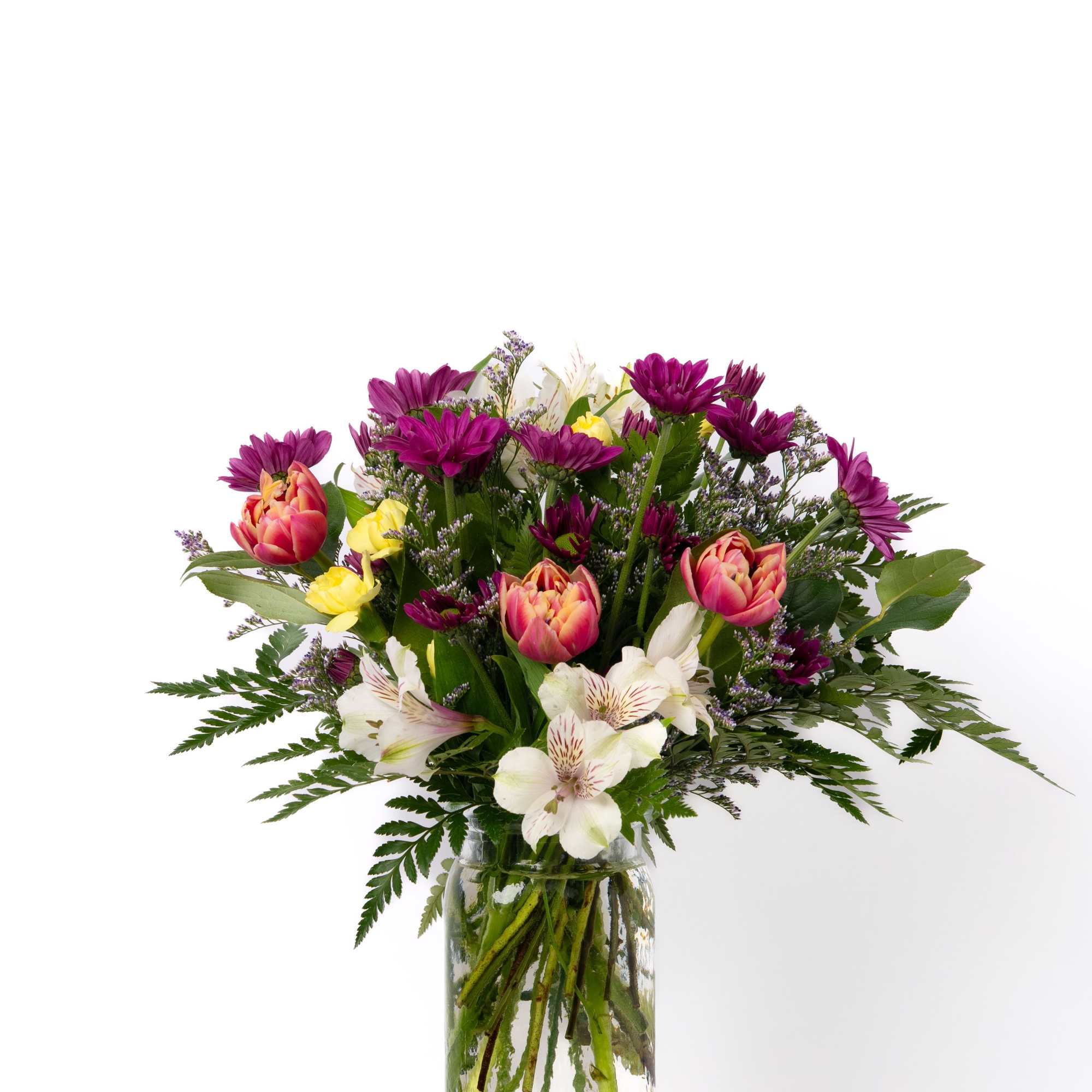 Mixed bouquet of purple daisies, pink tulips, and white blooms in a clear glass vase