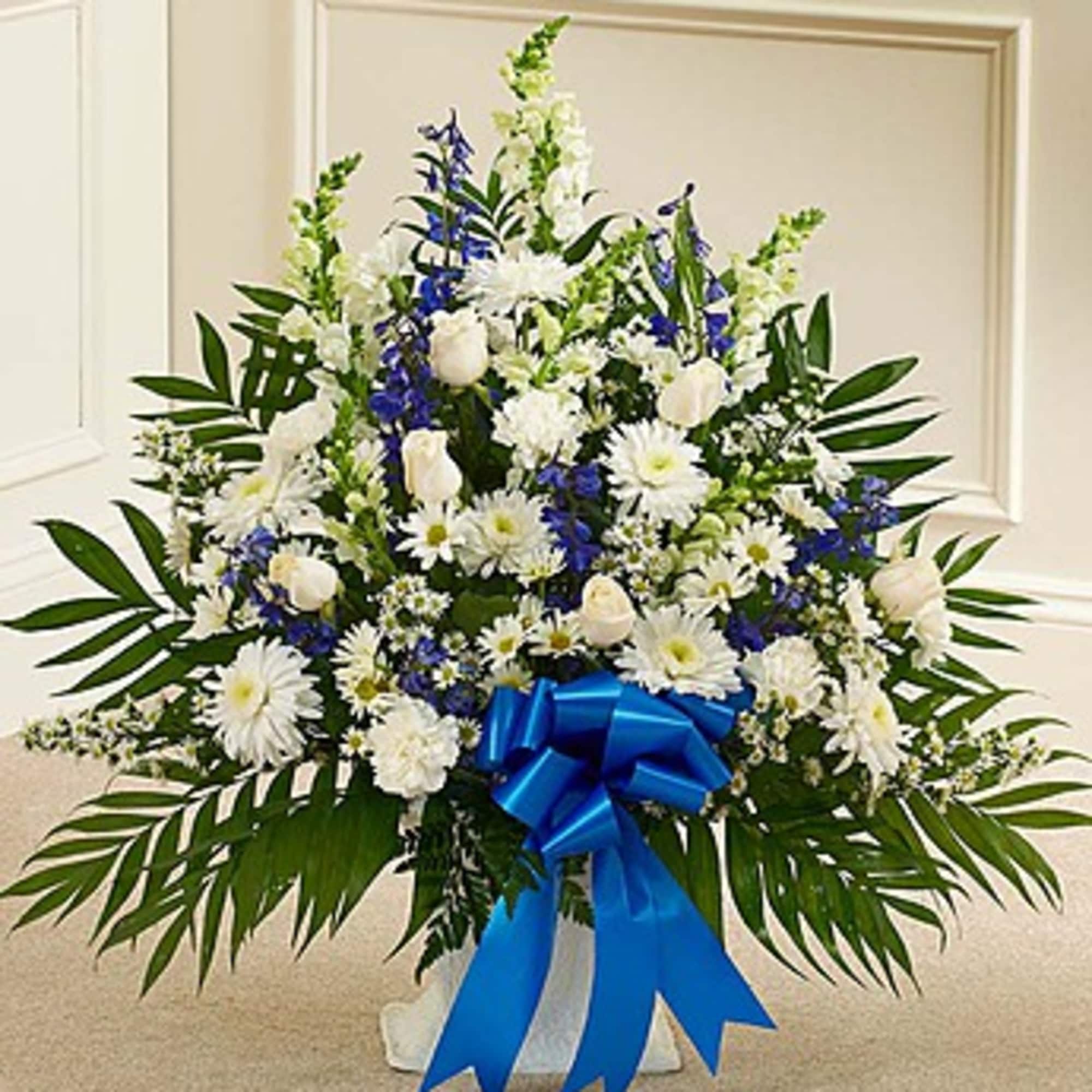 White and blue floral arrangement with a blue ribbon in a white container