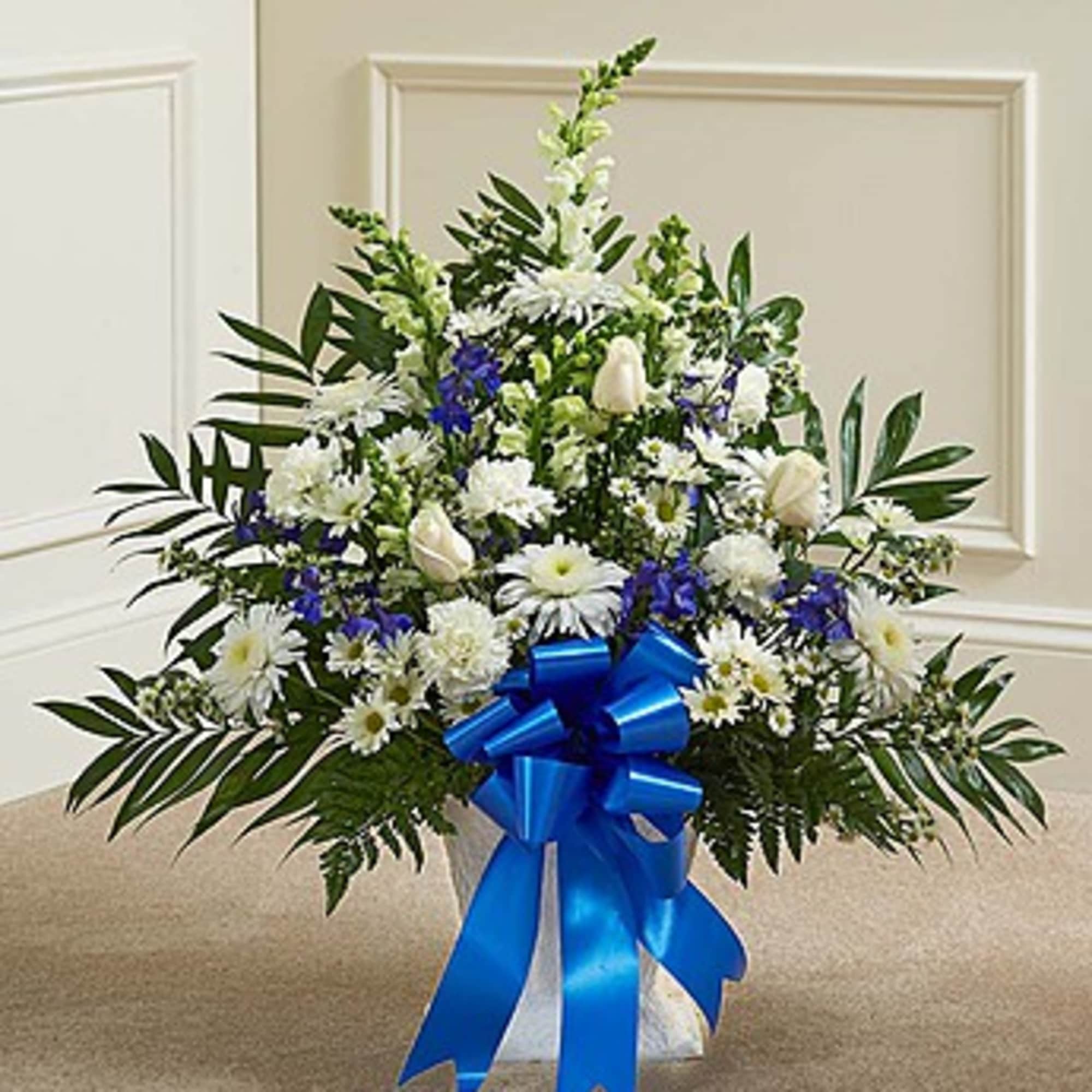 White and blue floral arrangement in a white container with a blue ribbon