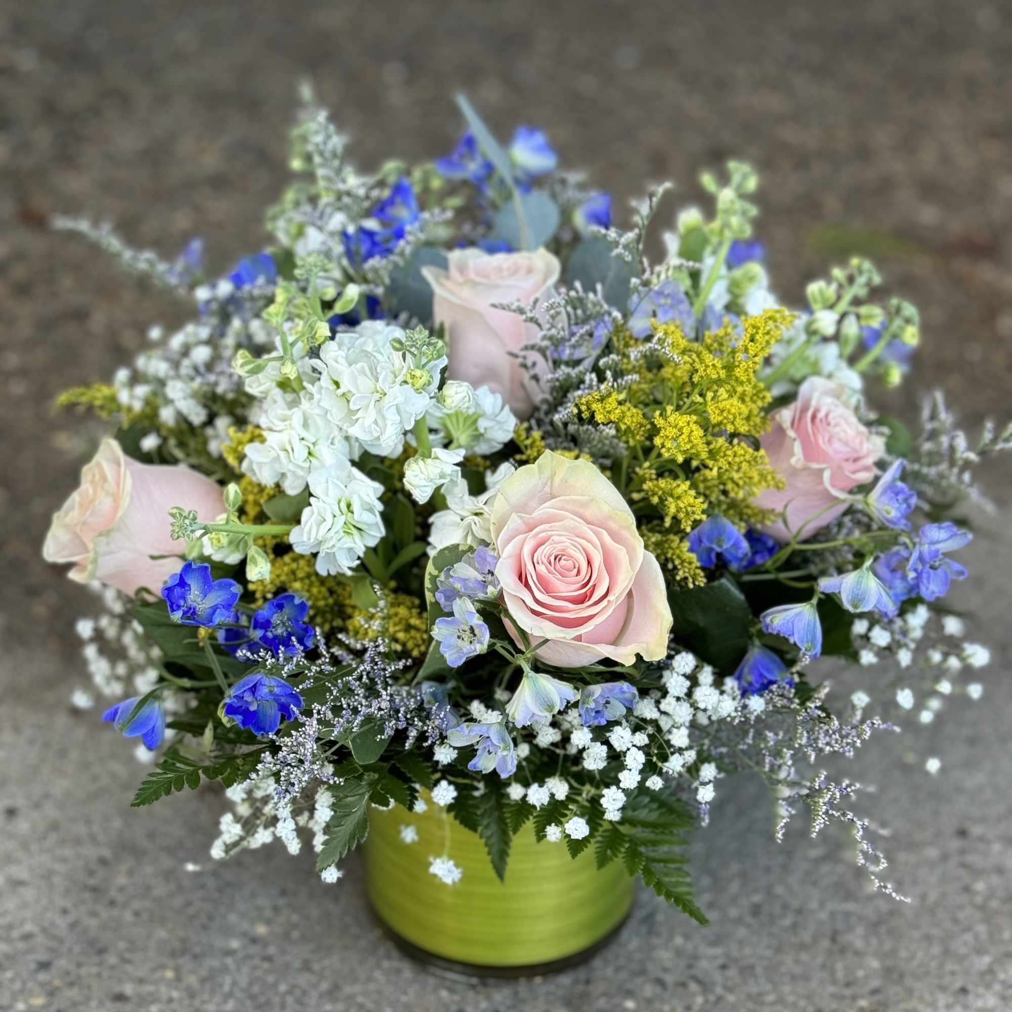 Mixed bouquet of pink roses, blue flowers, and white blooms in a green vase