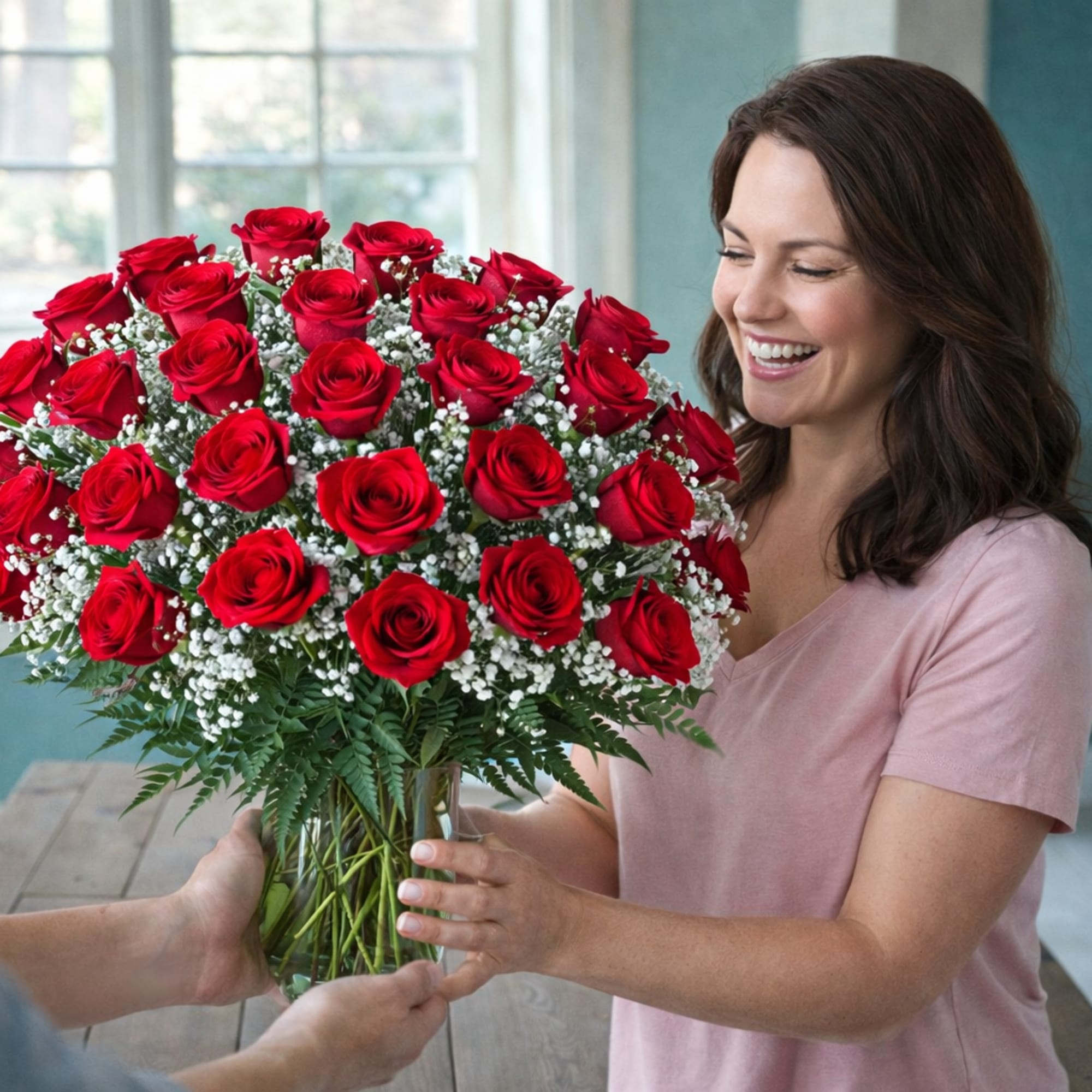 Large bouquet of red roses with white filler flowers in a clear glass vase being handed to a smiling woman