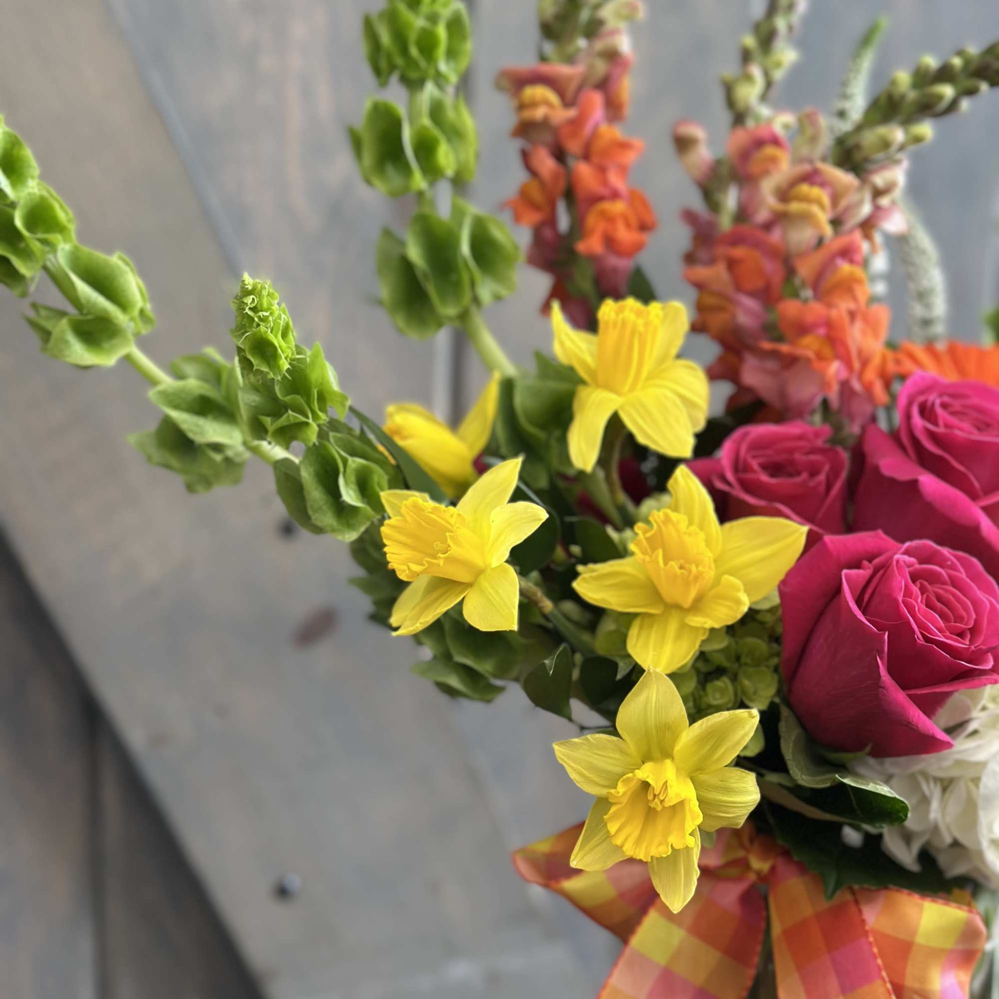 Bouquet with pink roses, yellow daffodils, and orange snapdragons tied with a plaid ribbon.