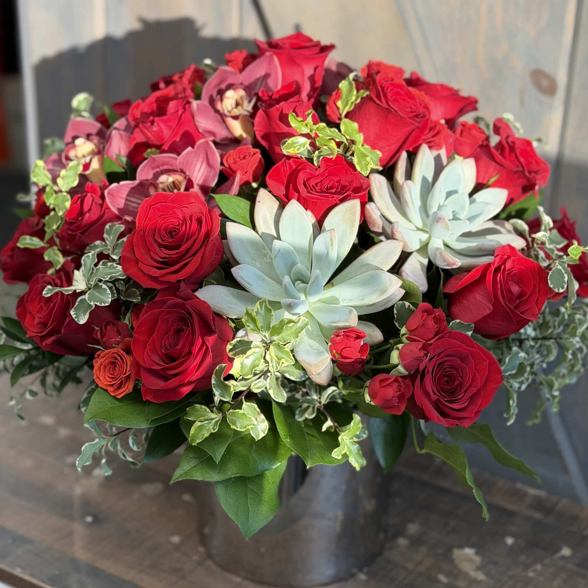 Red roses and pale succulents arranged in a dark vase