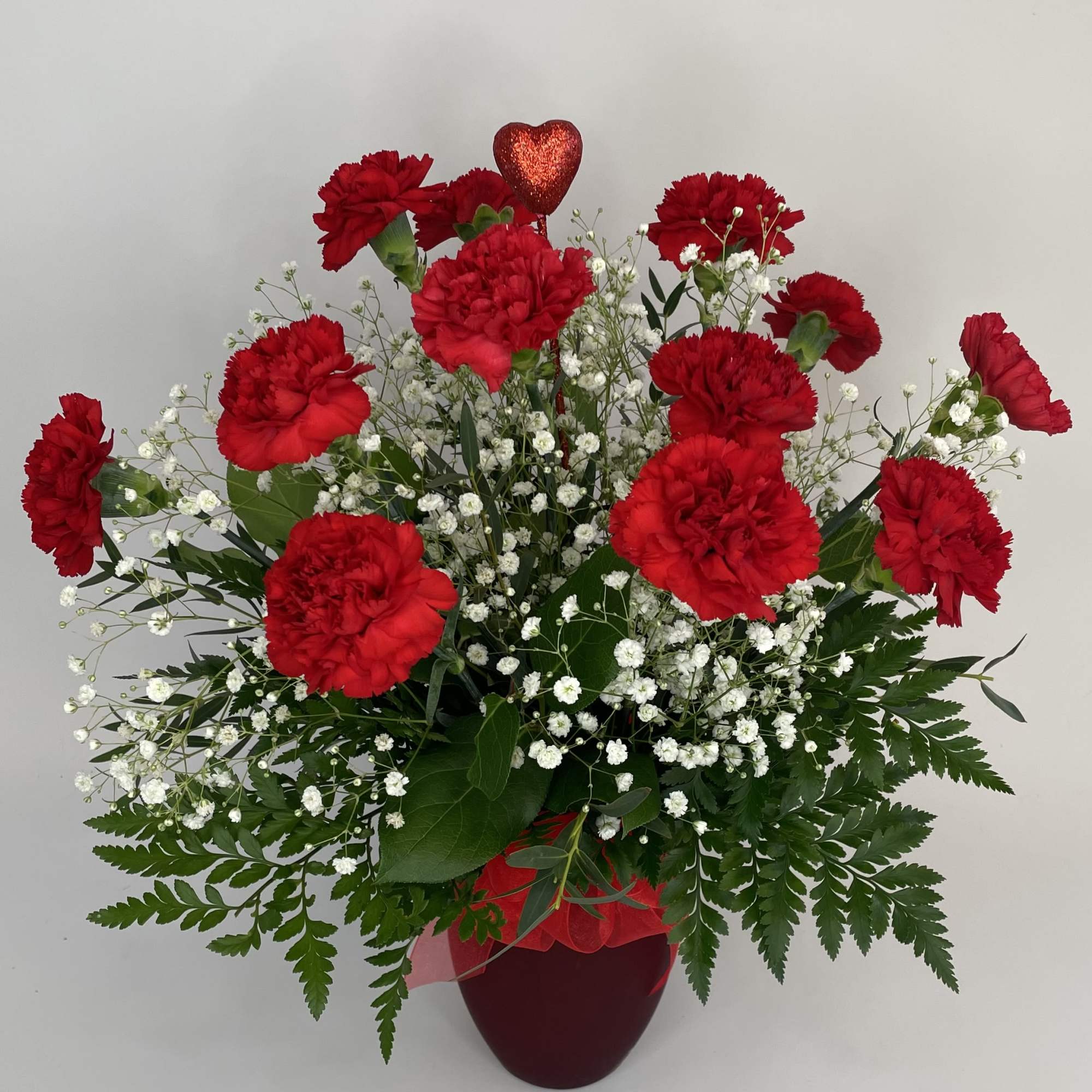 A dozen charming carnations arranged in a ruby red vase to showcase