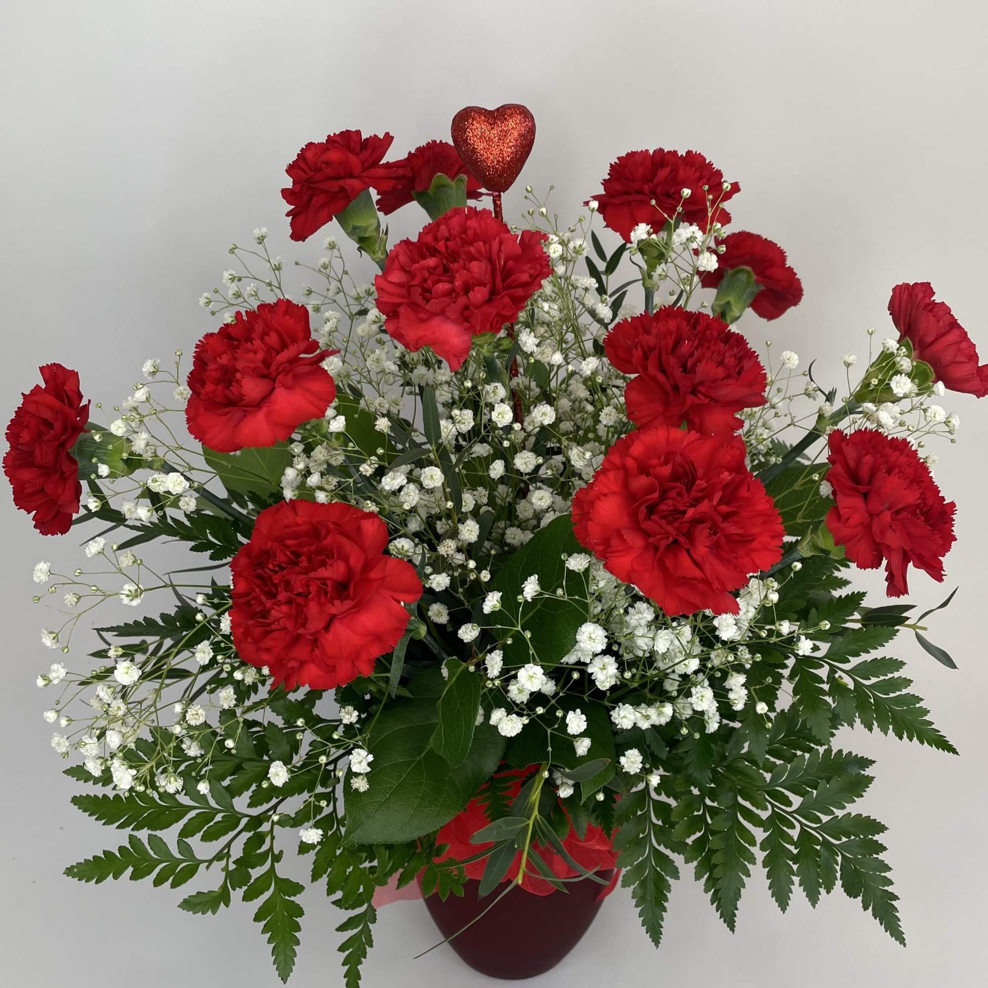 Red carnations with white baby's breath in a red vase and heart pick