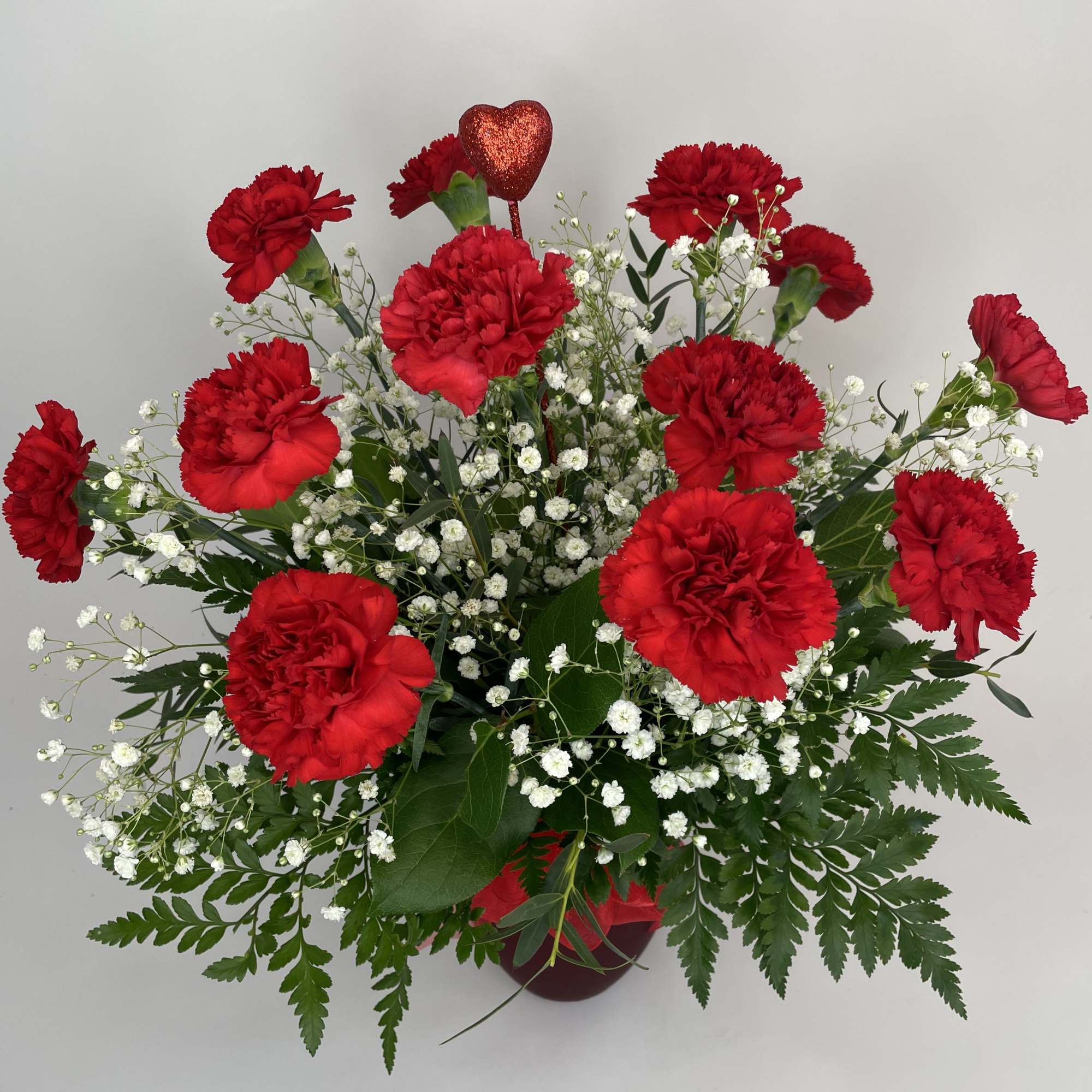 A dozen charming carnations arranged in a ruby red vase to showcase