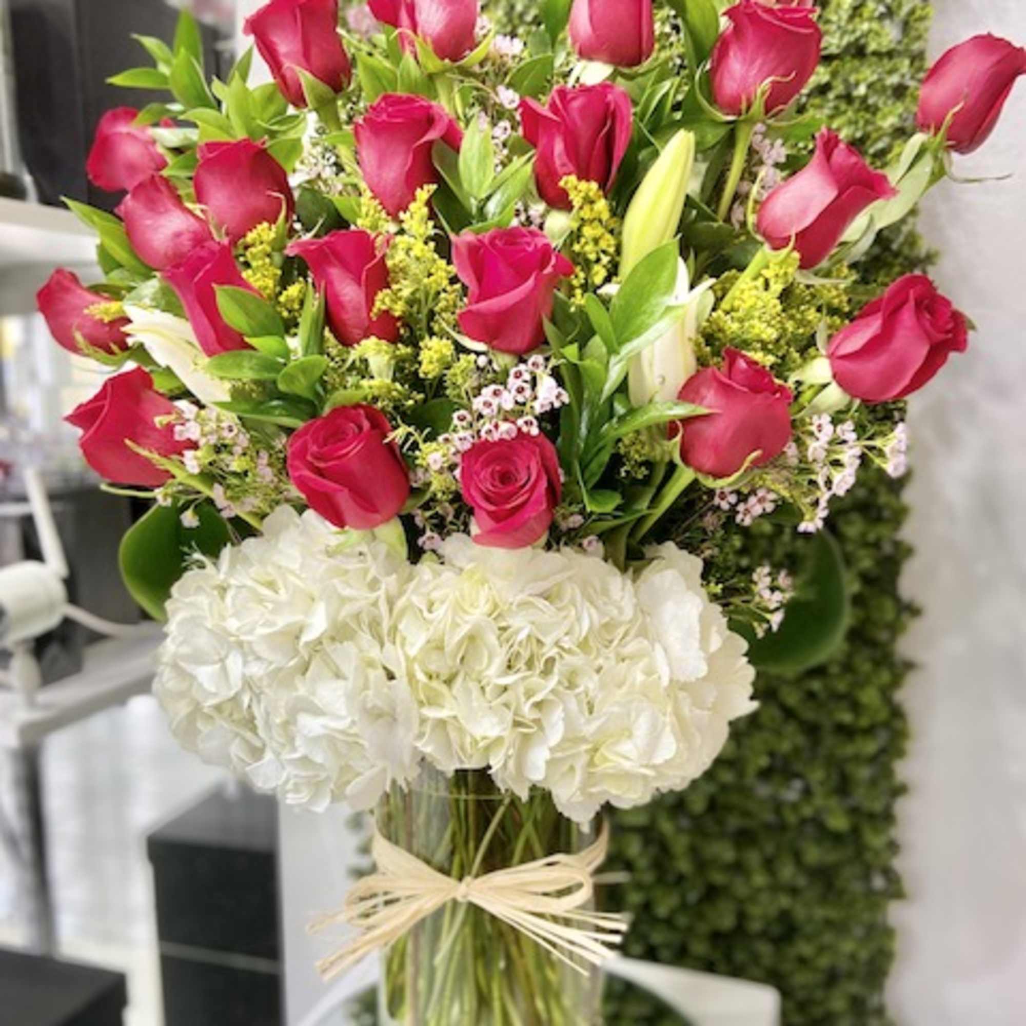 Tall arrangement of hot pink roses and white hydrangeas in a clear glass vase with raffia tie