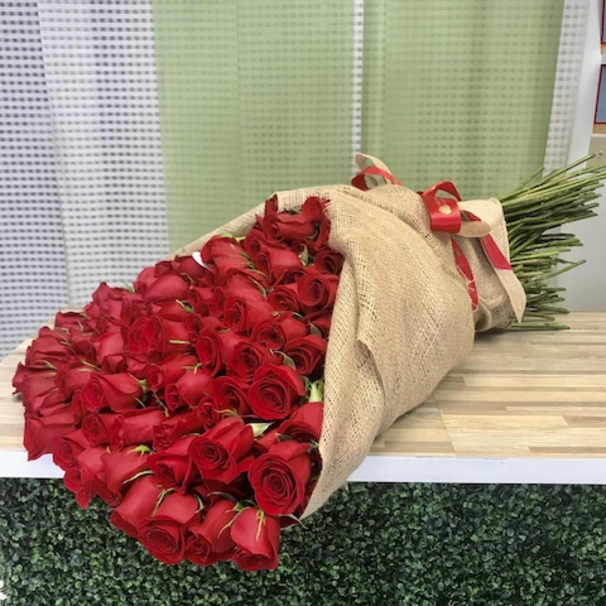 Large wrapped bouquet of long-stem red roses tied with a red ribbon
