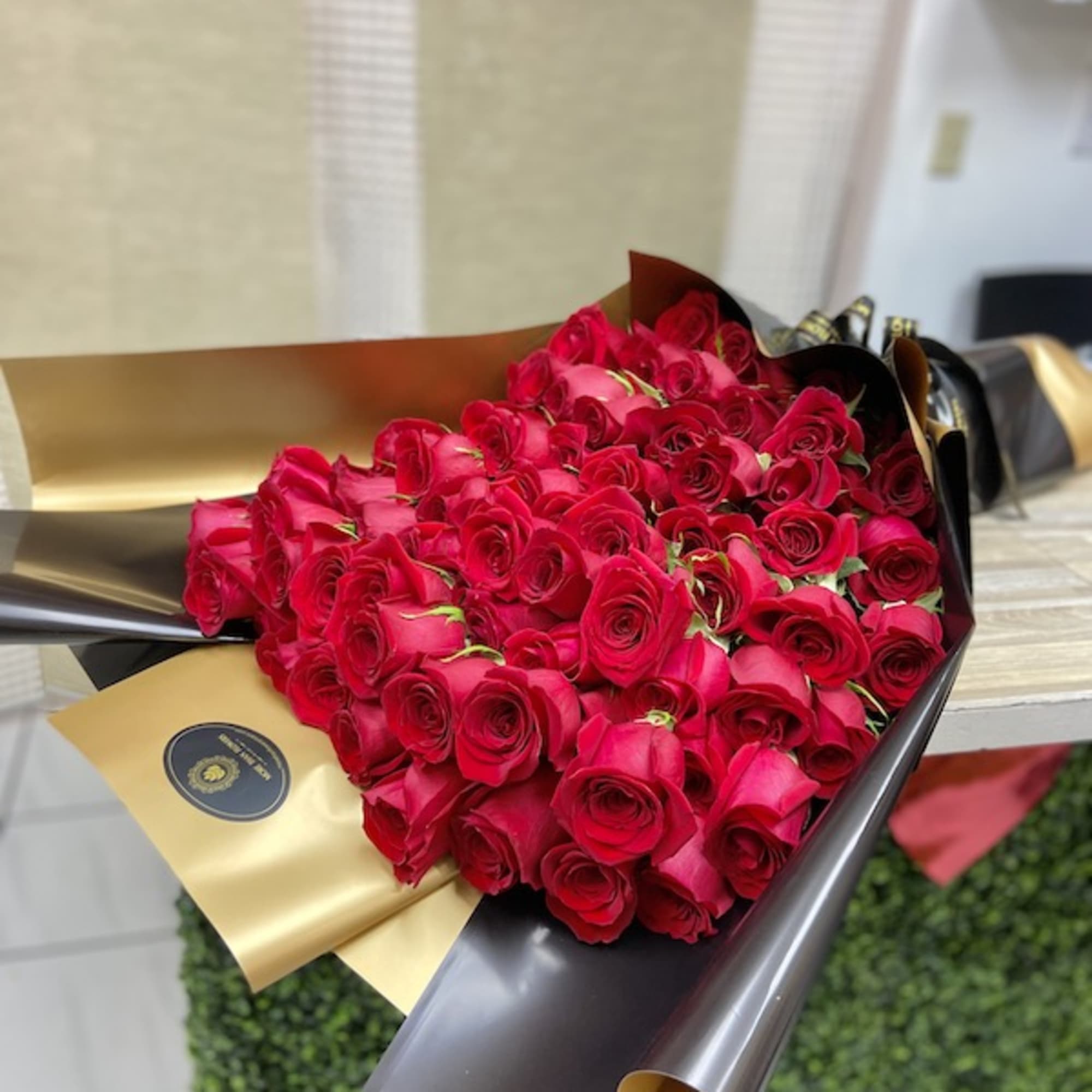 Large bouquet of tightly clustered red roses wrapped in glossy black and gold paper