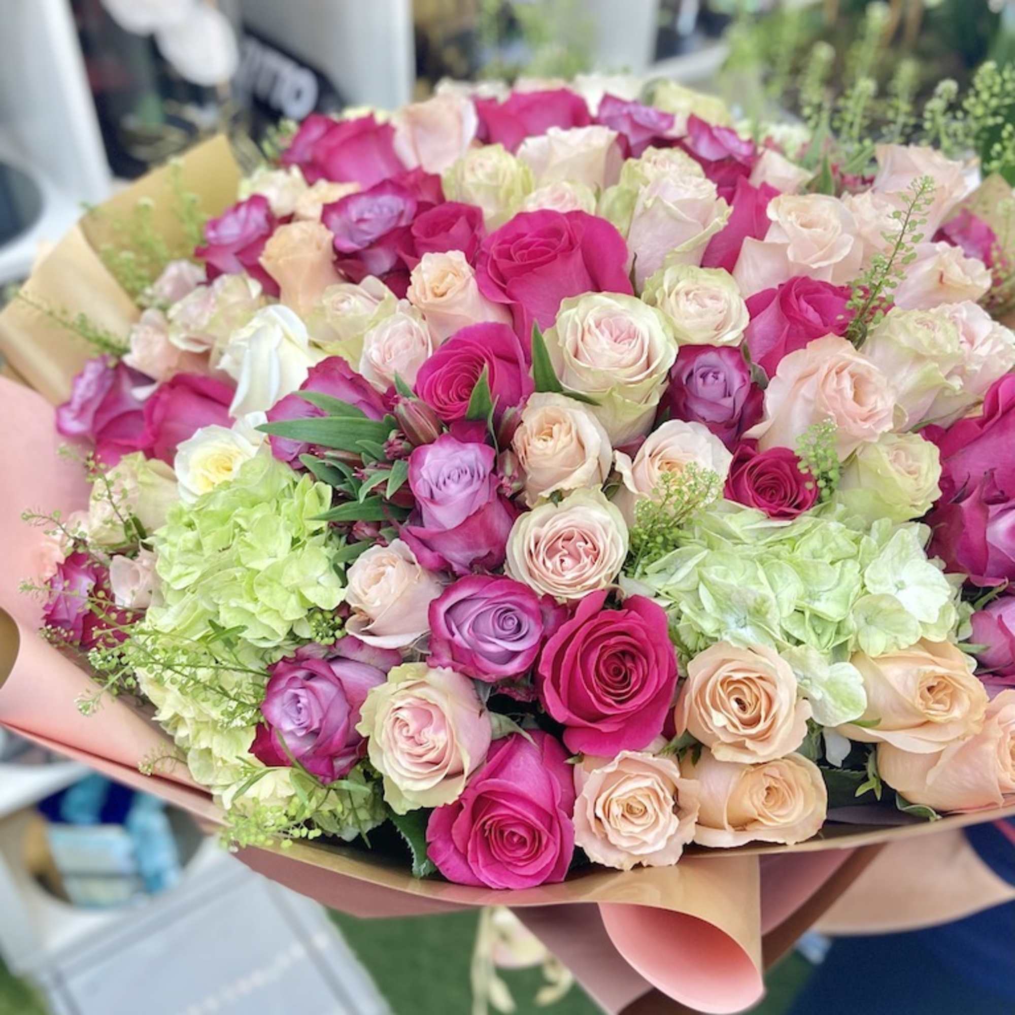 Large hand-tied bouquet of hot pink, peach, cream and lavender roses with green hydrangeas in pastel wrap
