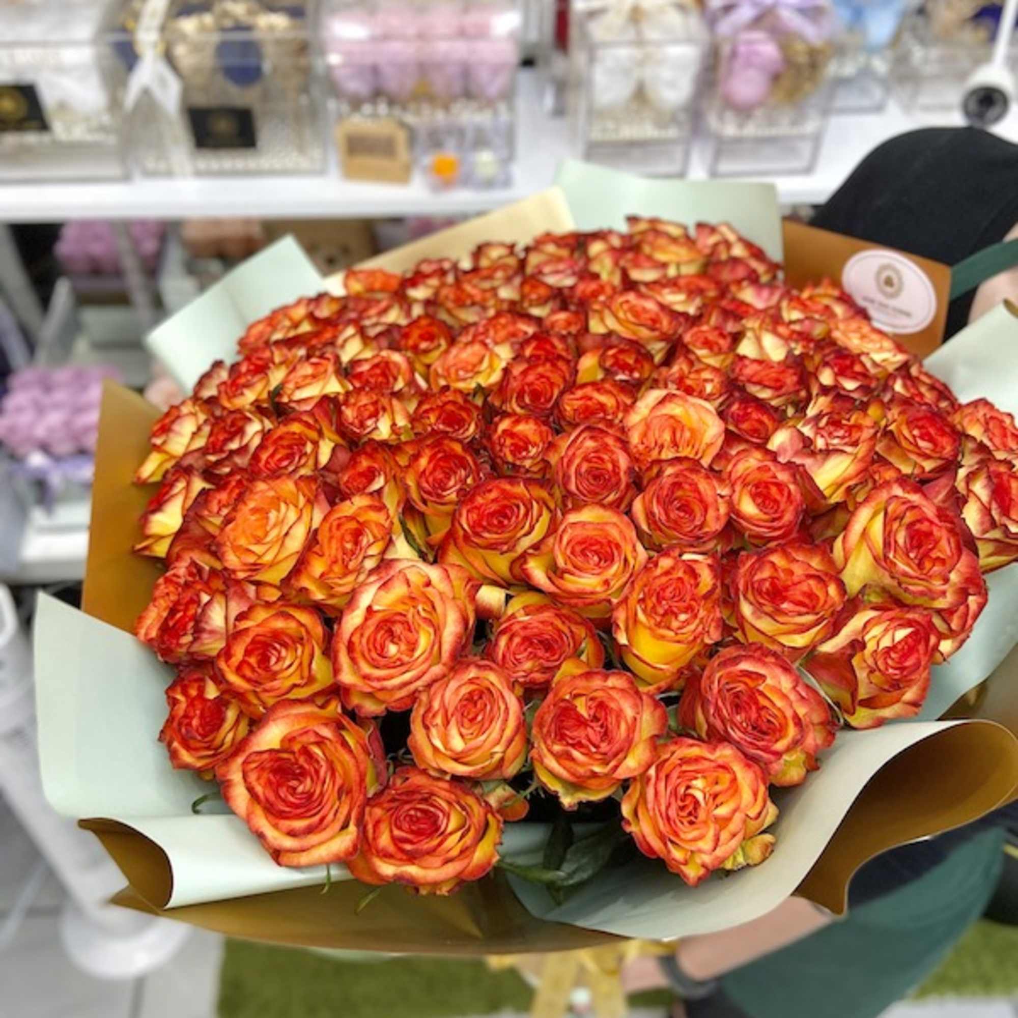 Large bouquet of orange and yellow roses wrapped in pale green and gold paper