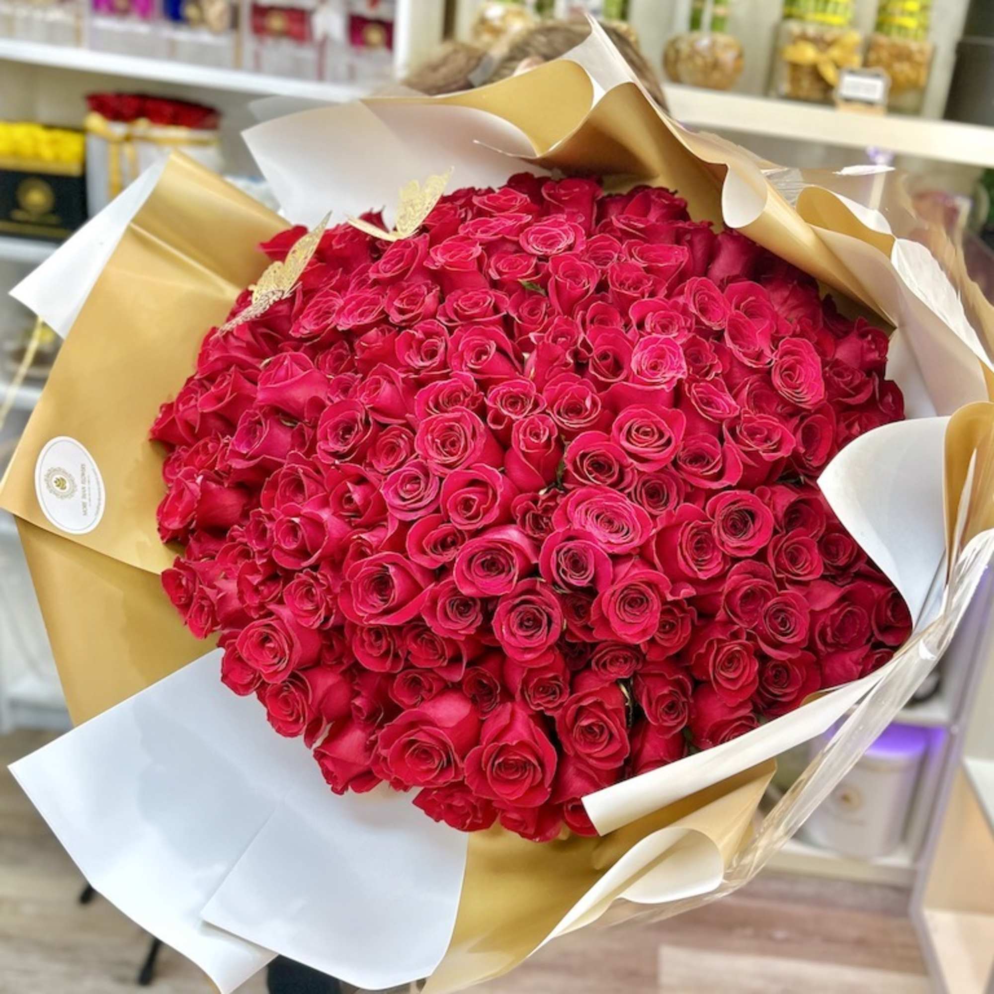 Large bouquet of hot pink roses wrapped in white and gold paper in a flower shop