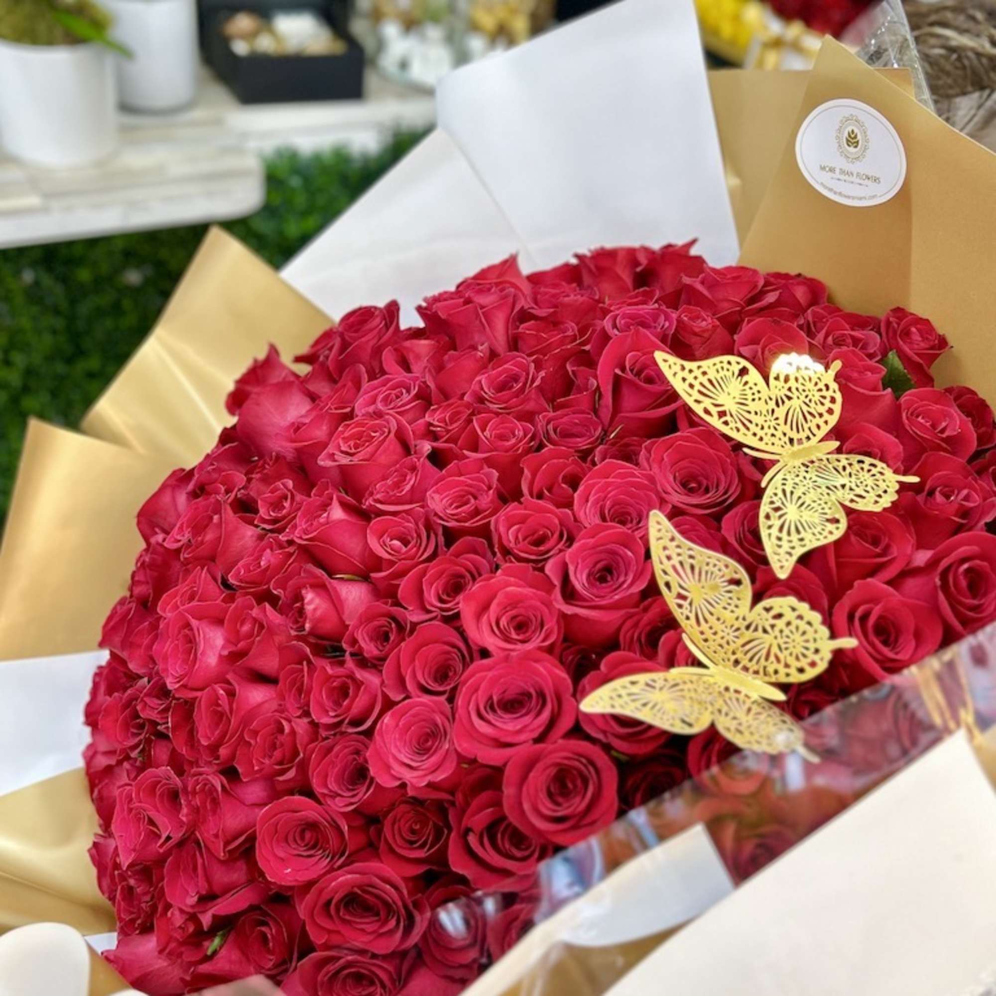 Large bouquet of tightly packed hot pink roses wrapped in white and gold paper with gold butterfly accents