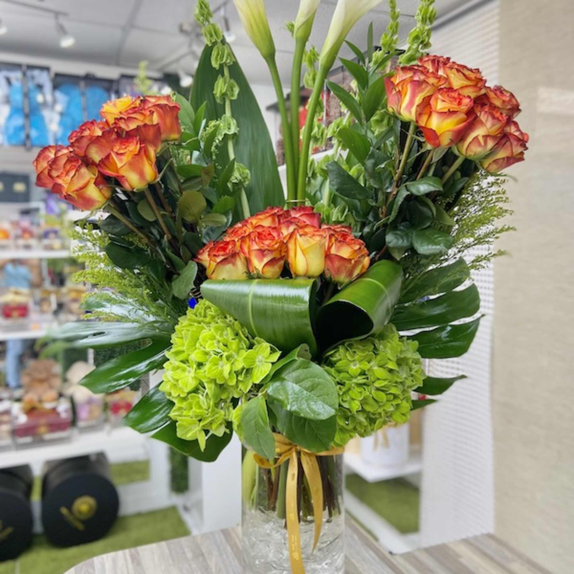 Tall arrangement of orange roses, white calla lilies, and green hydrangeas in a clear glass vase