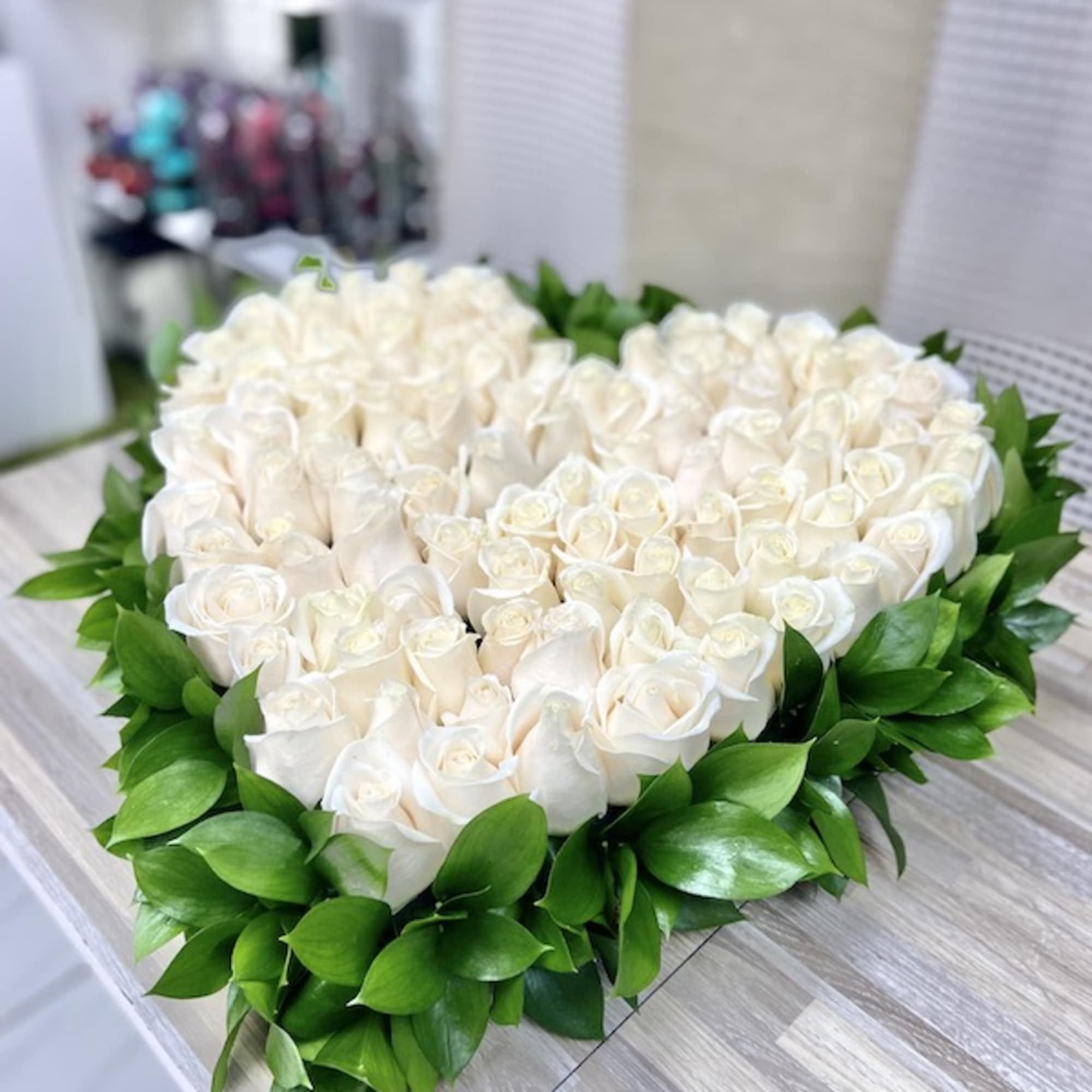 Heart-shaped arrangement of white roses framed with bright green foliage on a wooden table