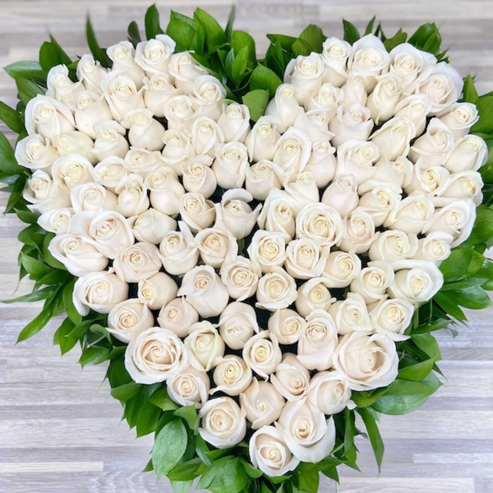 Heart-shaped arrangement of white roses edged with bright green foliage