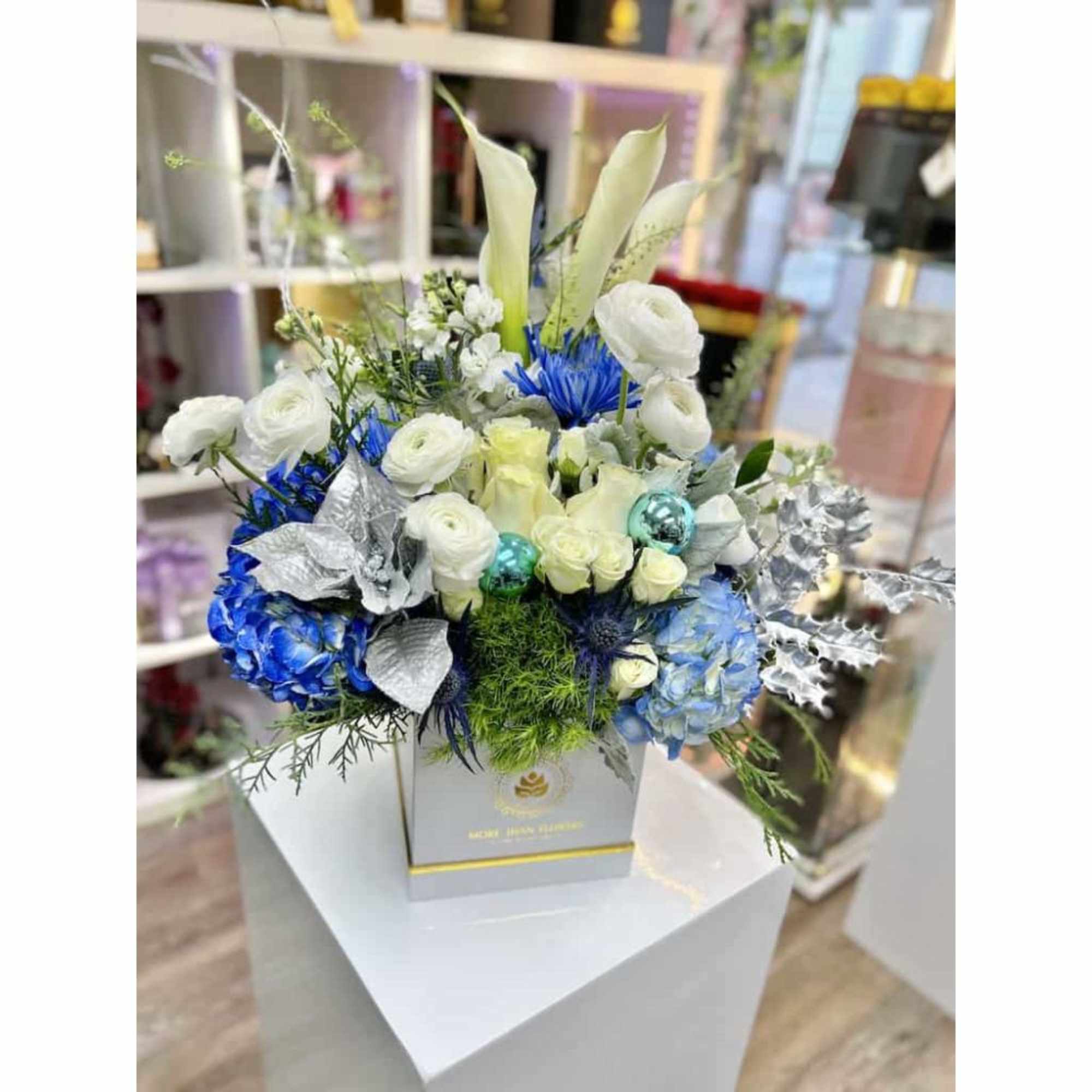 White and blue flower arrangement with calla lilies and roses in a square box with silver leaves and ornaments