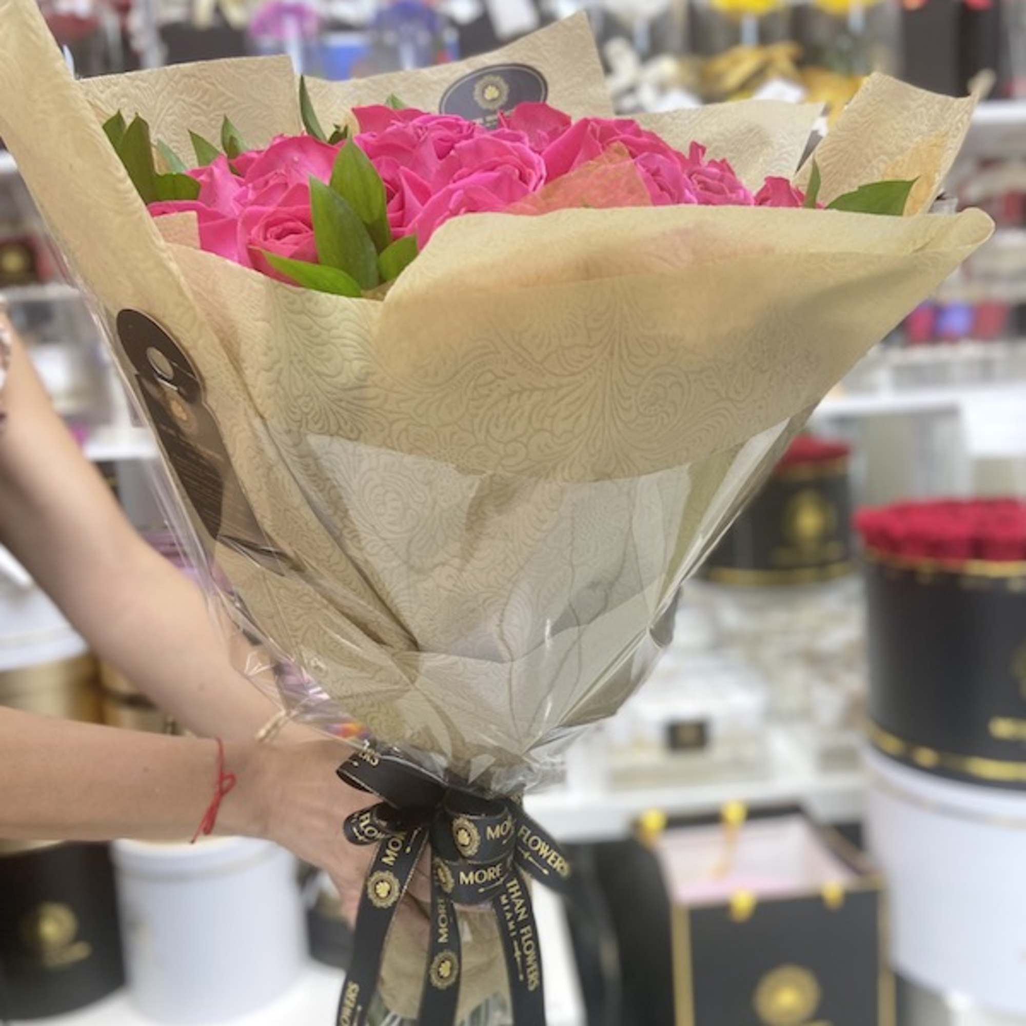Bouquet of bright pink roses wrapped in patterned beige paper and tied with a black logo ribbon