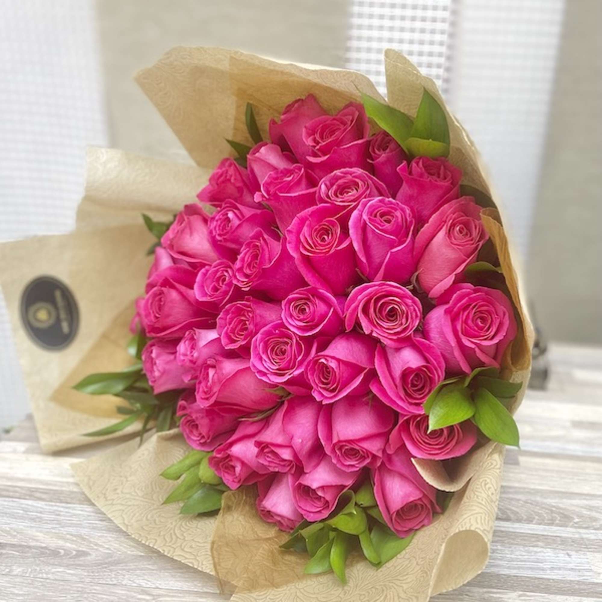 Bouquet of bright pink roses wrapped in tan patterned paper with touches of green foliage