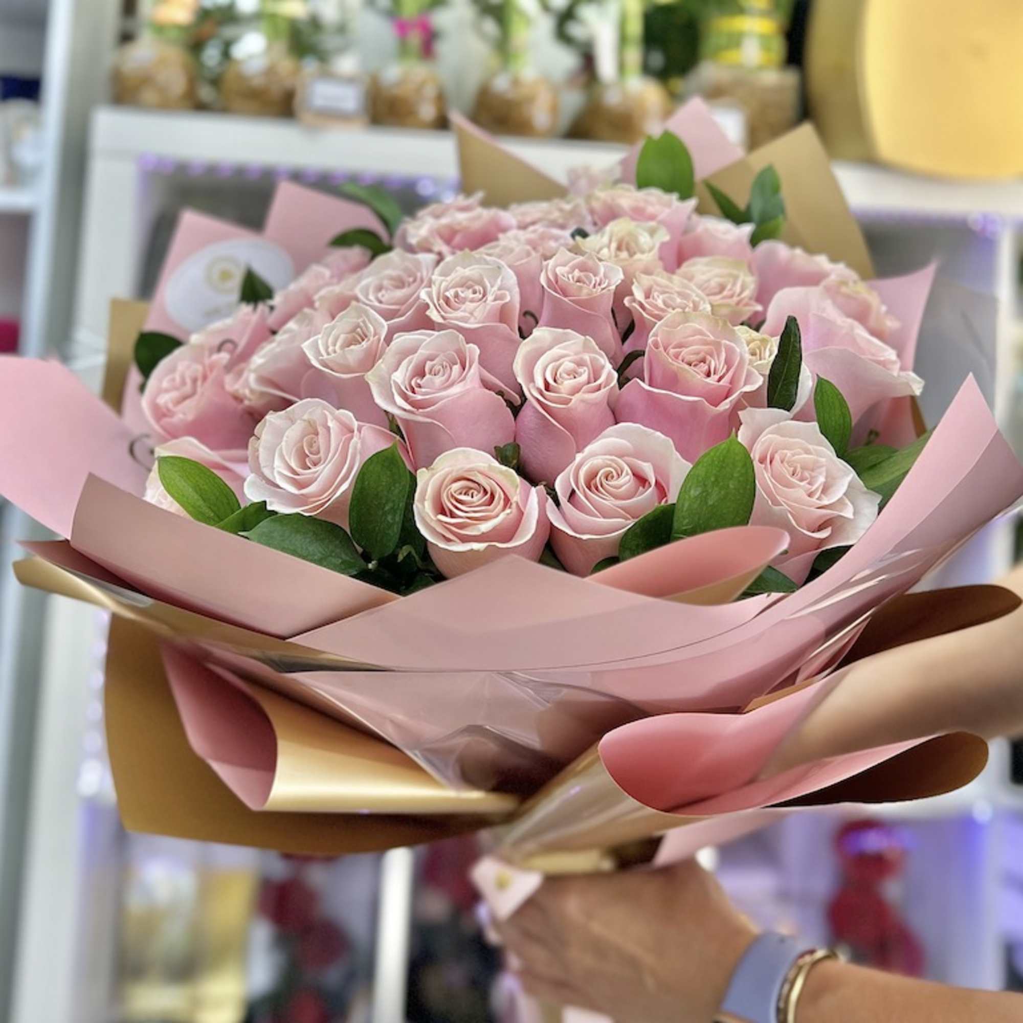 Large bouquet of light pink roses wrapped in pink and gold paper, held in one hand