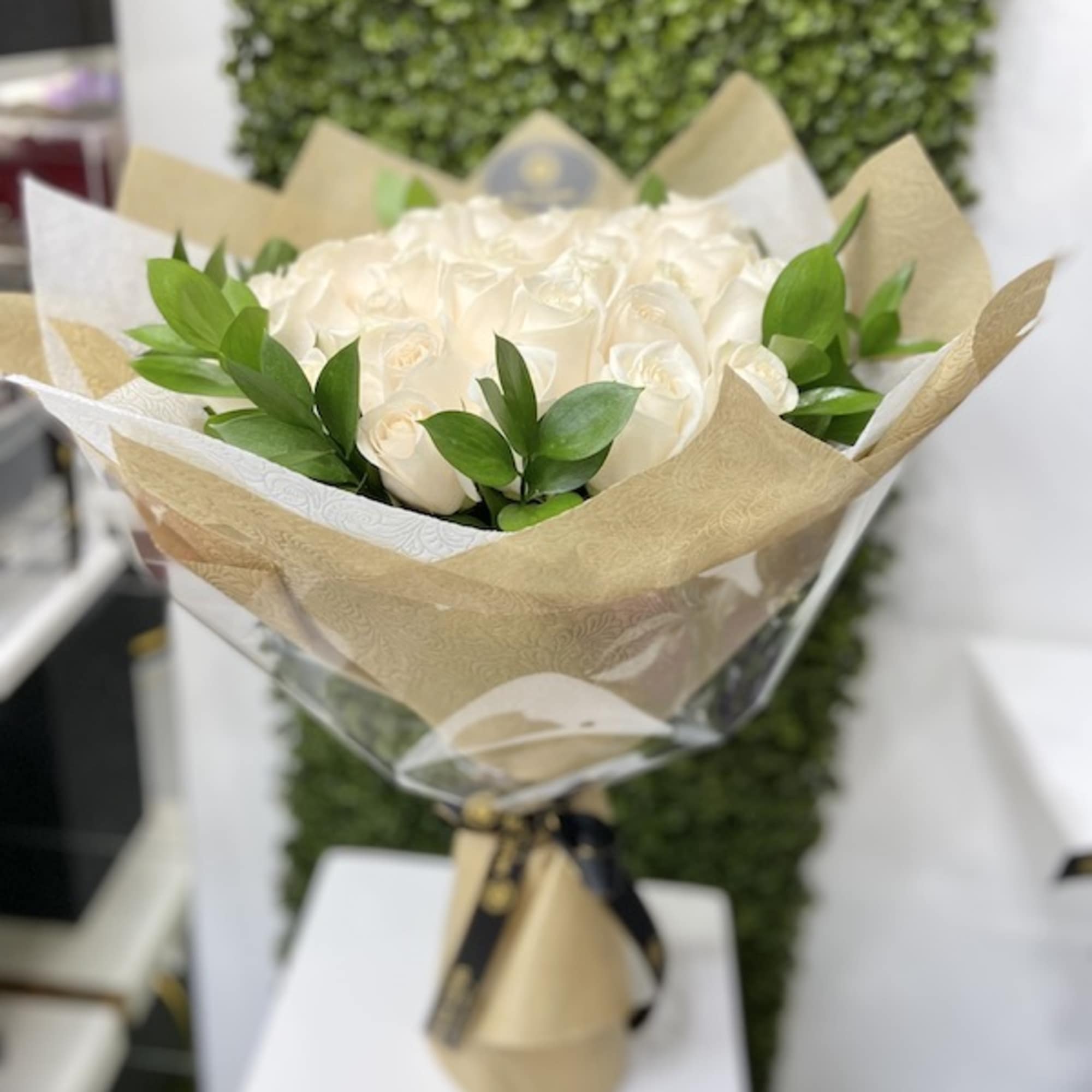 Hand-tied bouquet of white roses with green foliage wrapped in tan and white paper