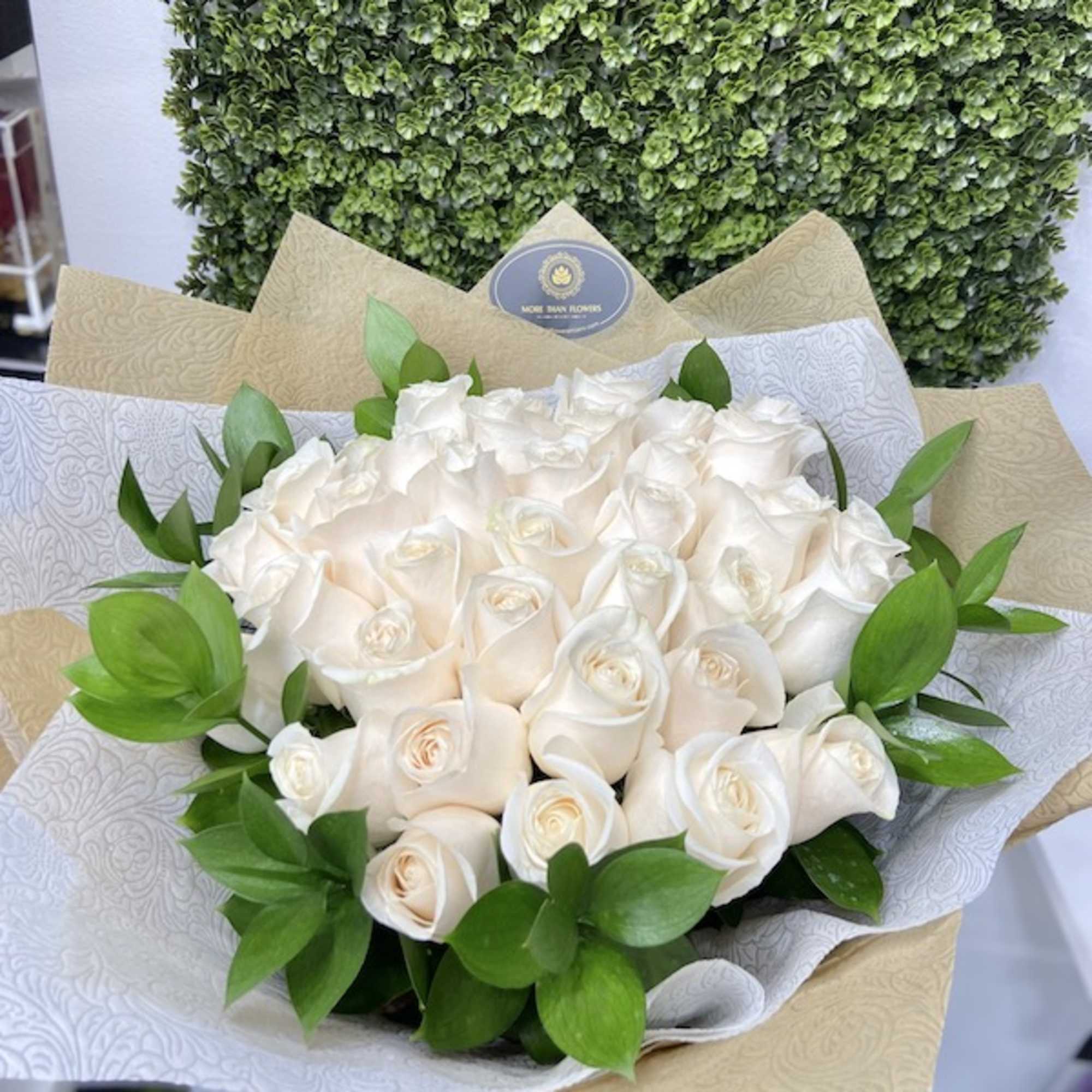 Bouquet of cream-colored roses wrapped in patterned white and kraft paper with a bow.