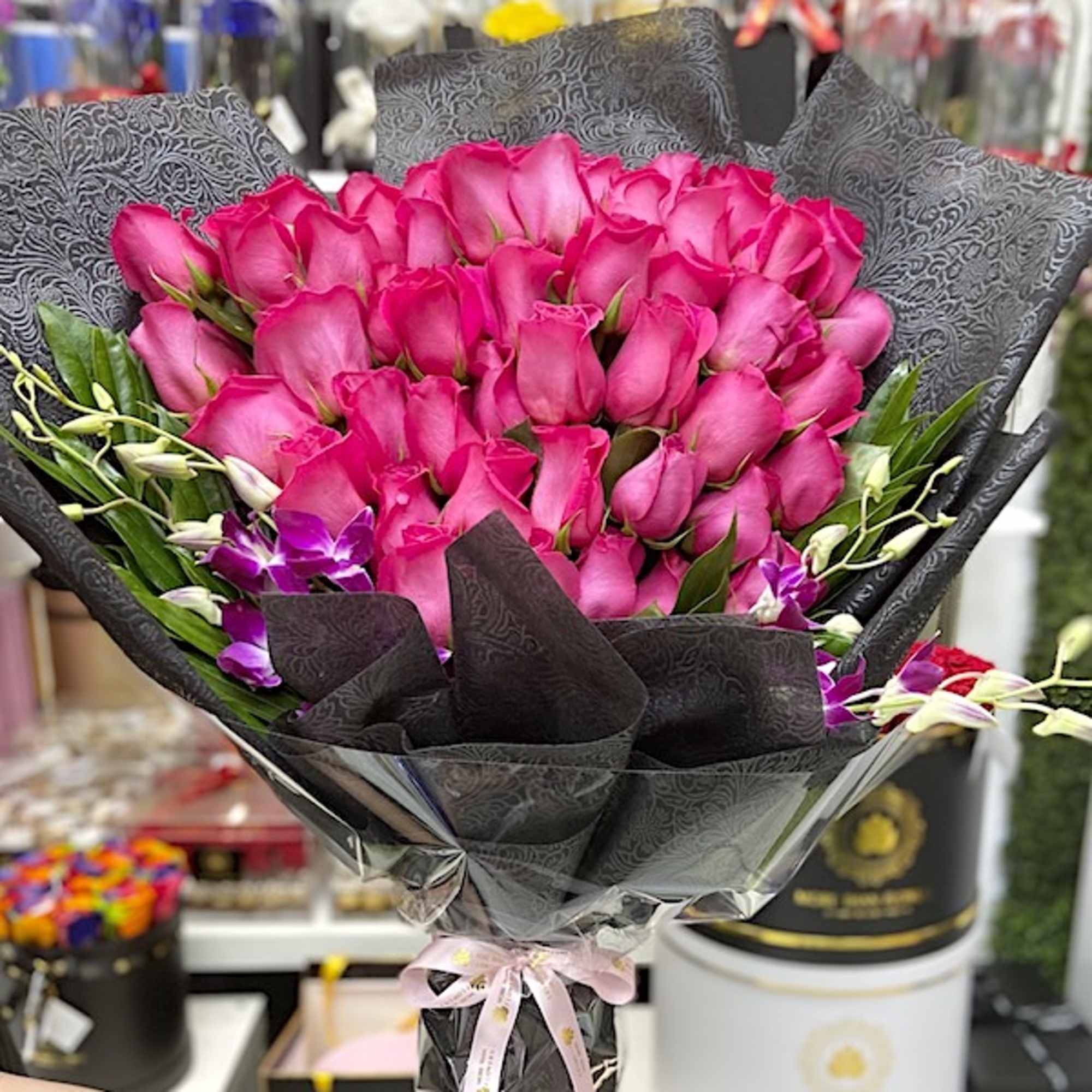 Large bouquet of bright pink roses with purple orchids wrapped in black paper.