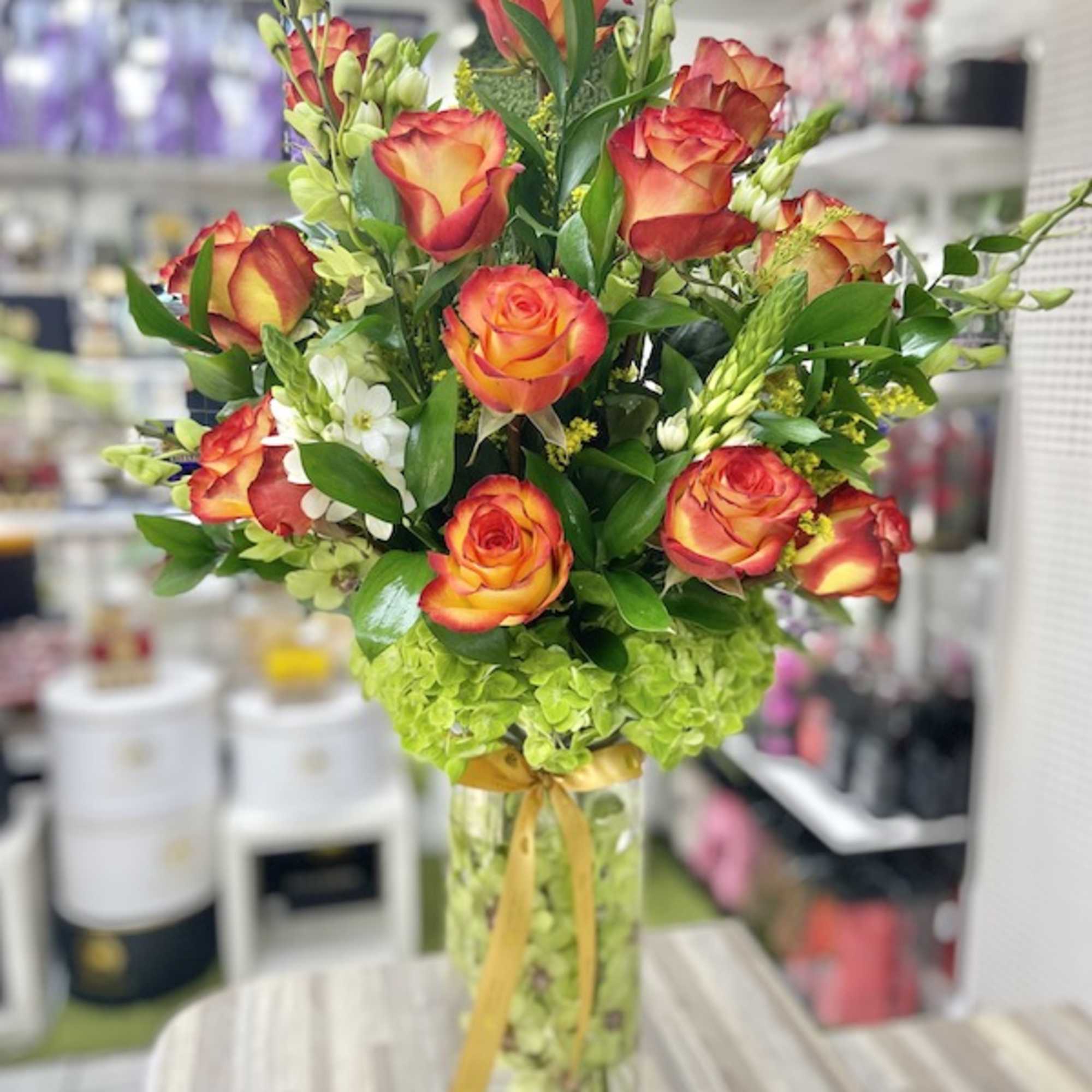 Tall arrangement of orange and yellow roses with green hydrangeas in a clear glass vase