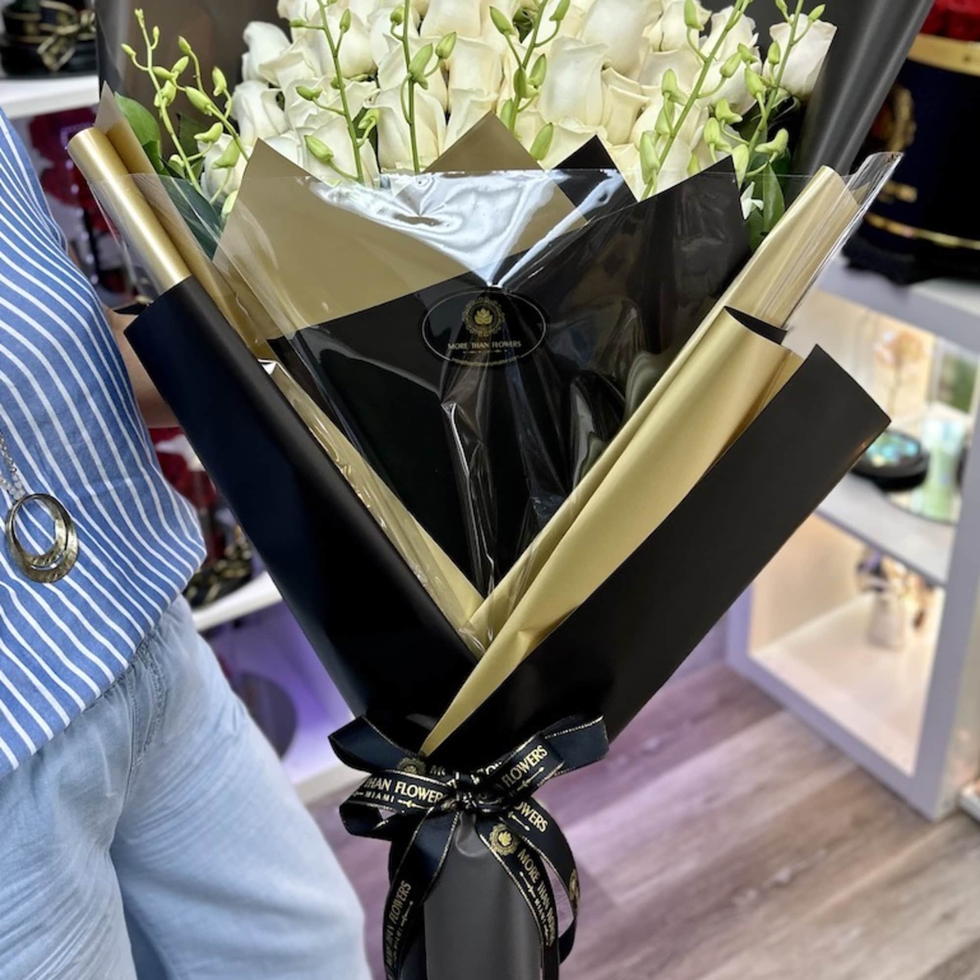 Hand-tied bouquet of white roses with delicate buds wrapped in black and gold paper.