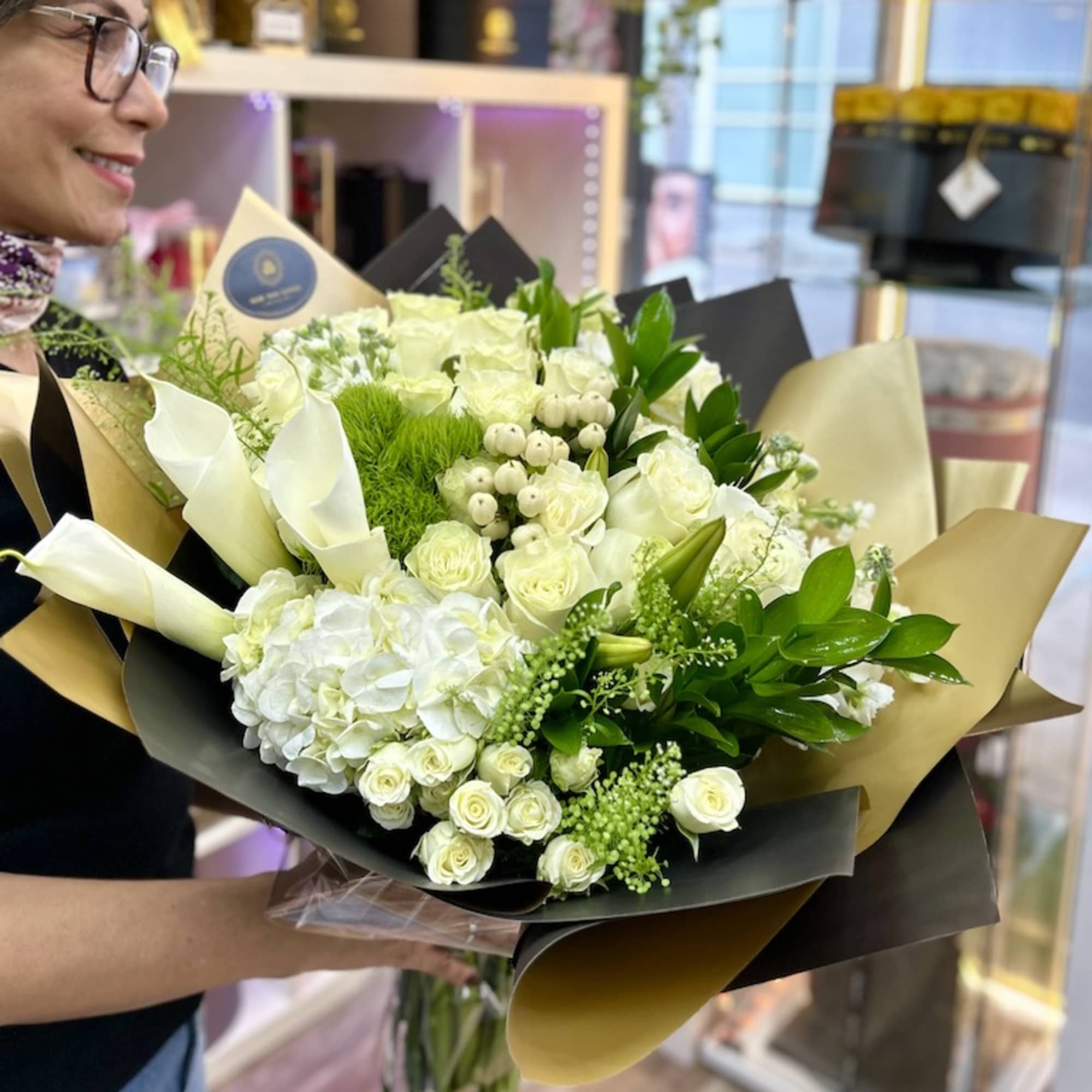 Large hand-tied bouquet of white roses, hydrangeas, and calla lilies wrapped in black and gold paper