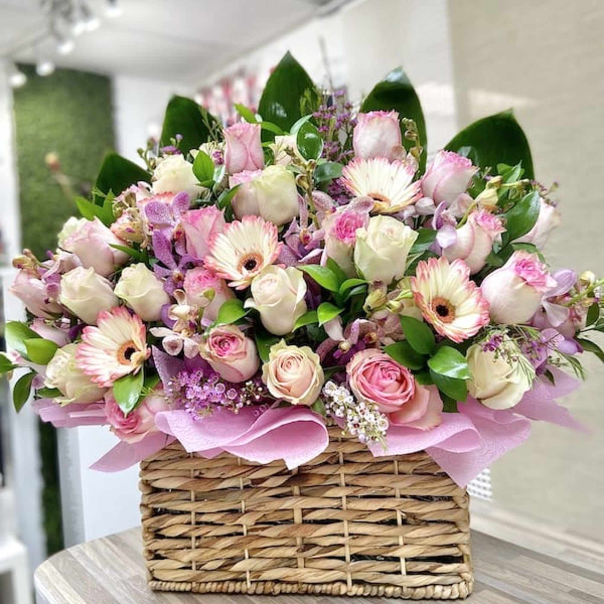 Pink and white rose and gerbera daisy arrangement in a wicker basket with pink wrap