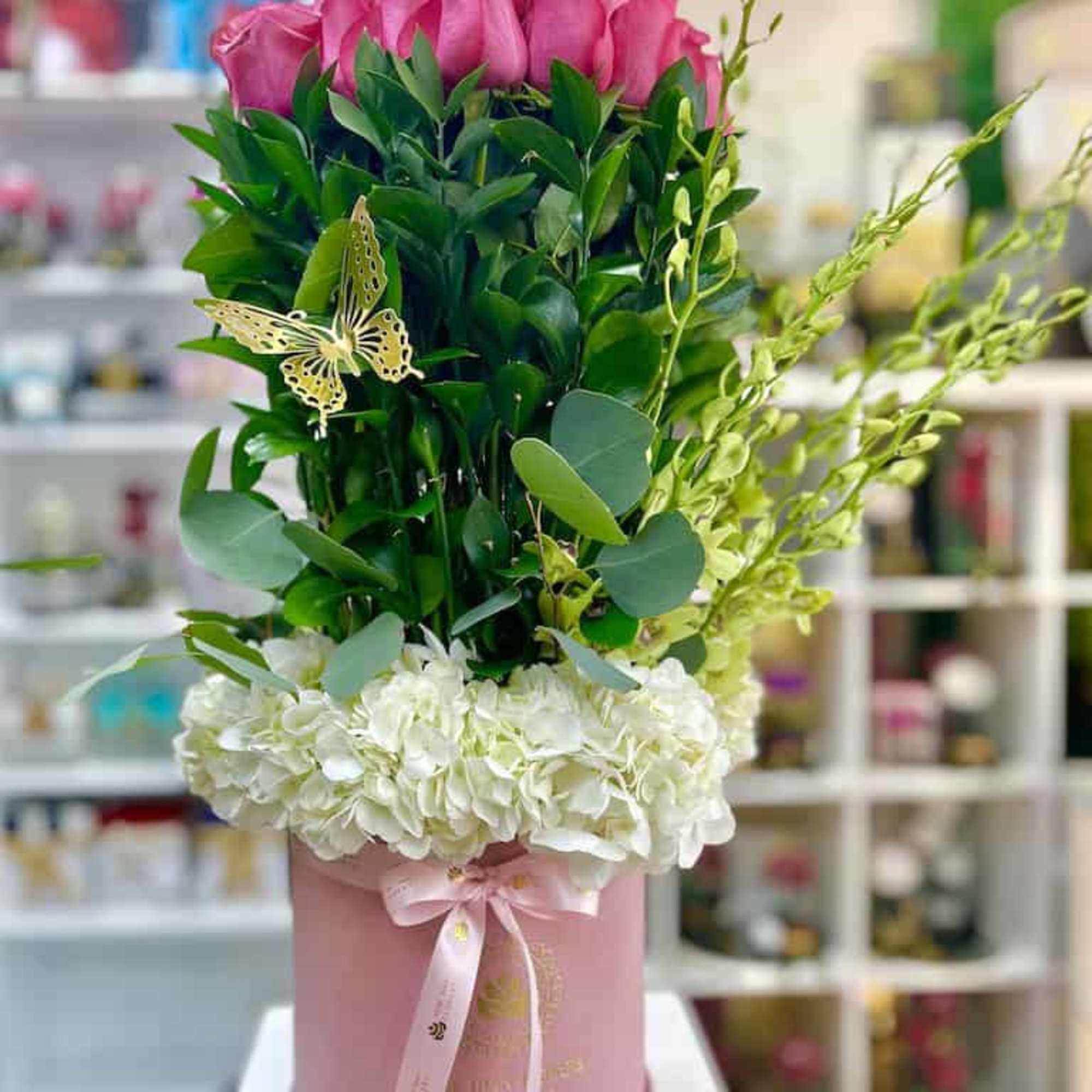 Tall arrangement of hot pink roses, greenery, and white hydrangeas in a pink hatbox with ribbon.