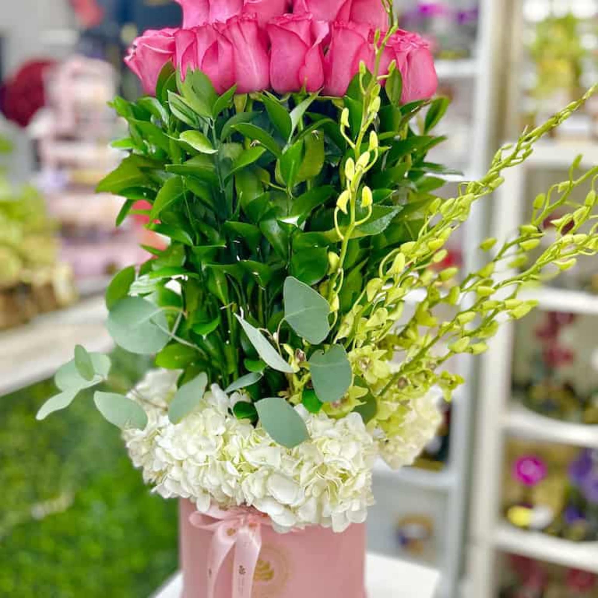 Tall column of pink roses rising from greenery with white hydrangeas in a pink hat box
