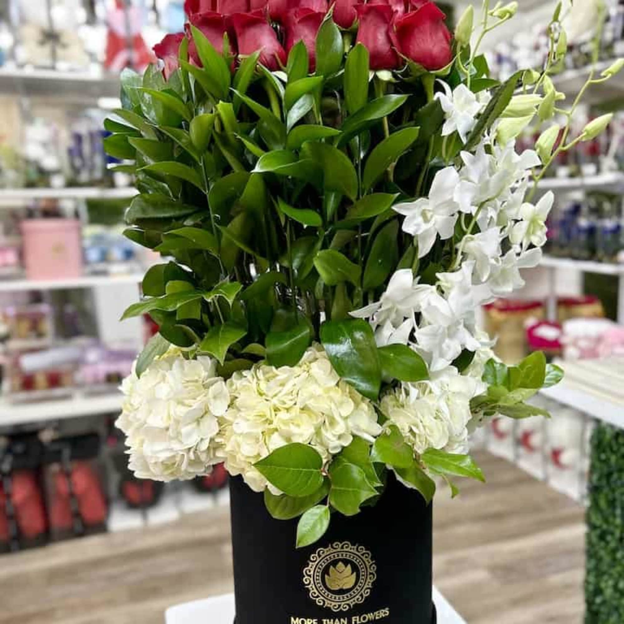 Tall arrangement of red roses, white orchids, and ivory hydrangeas in a black hatbox container