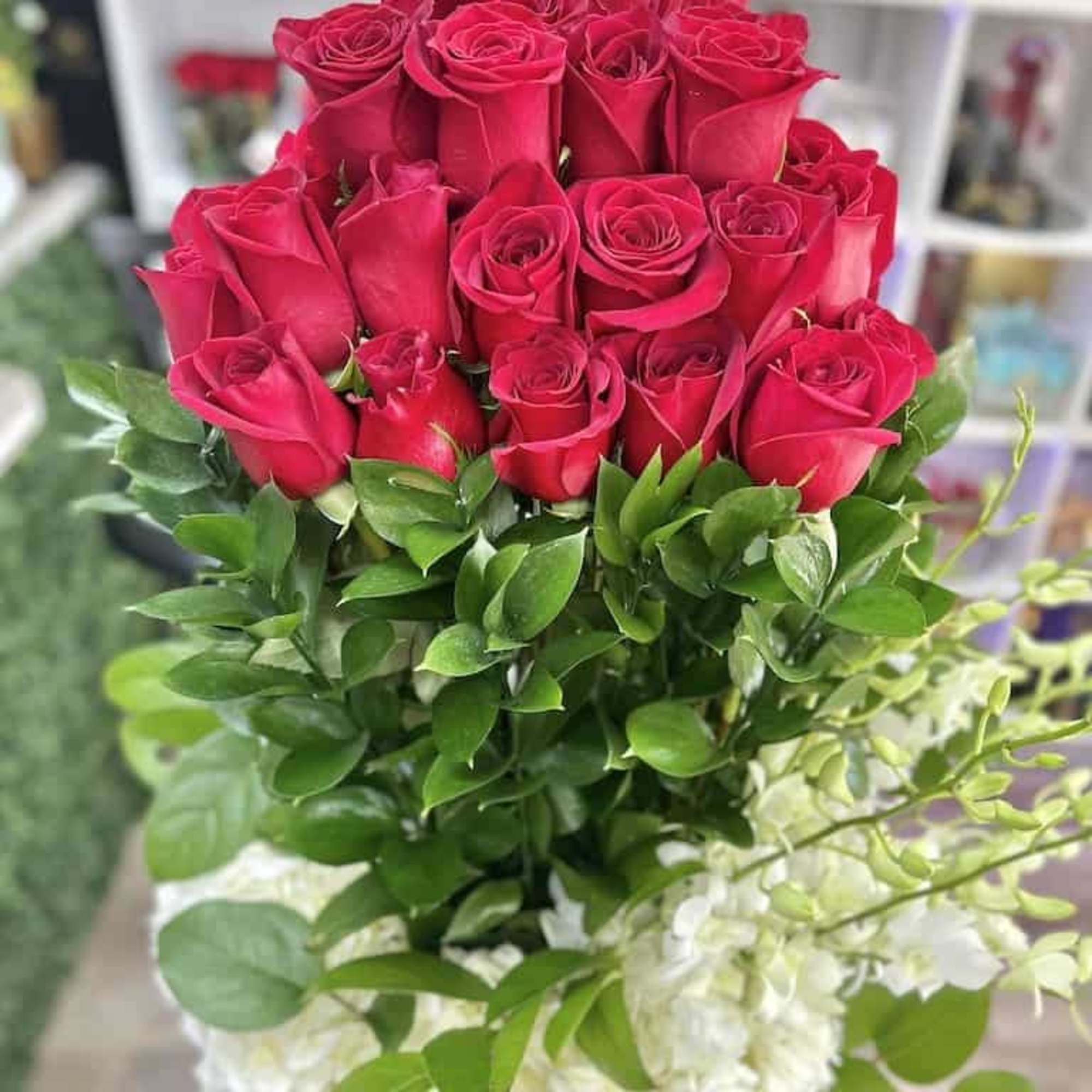 Tall arrangement of red roses above a base of white hydrangeas in a container