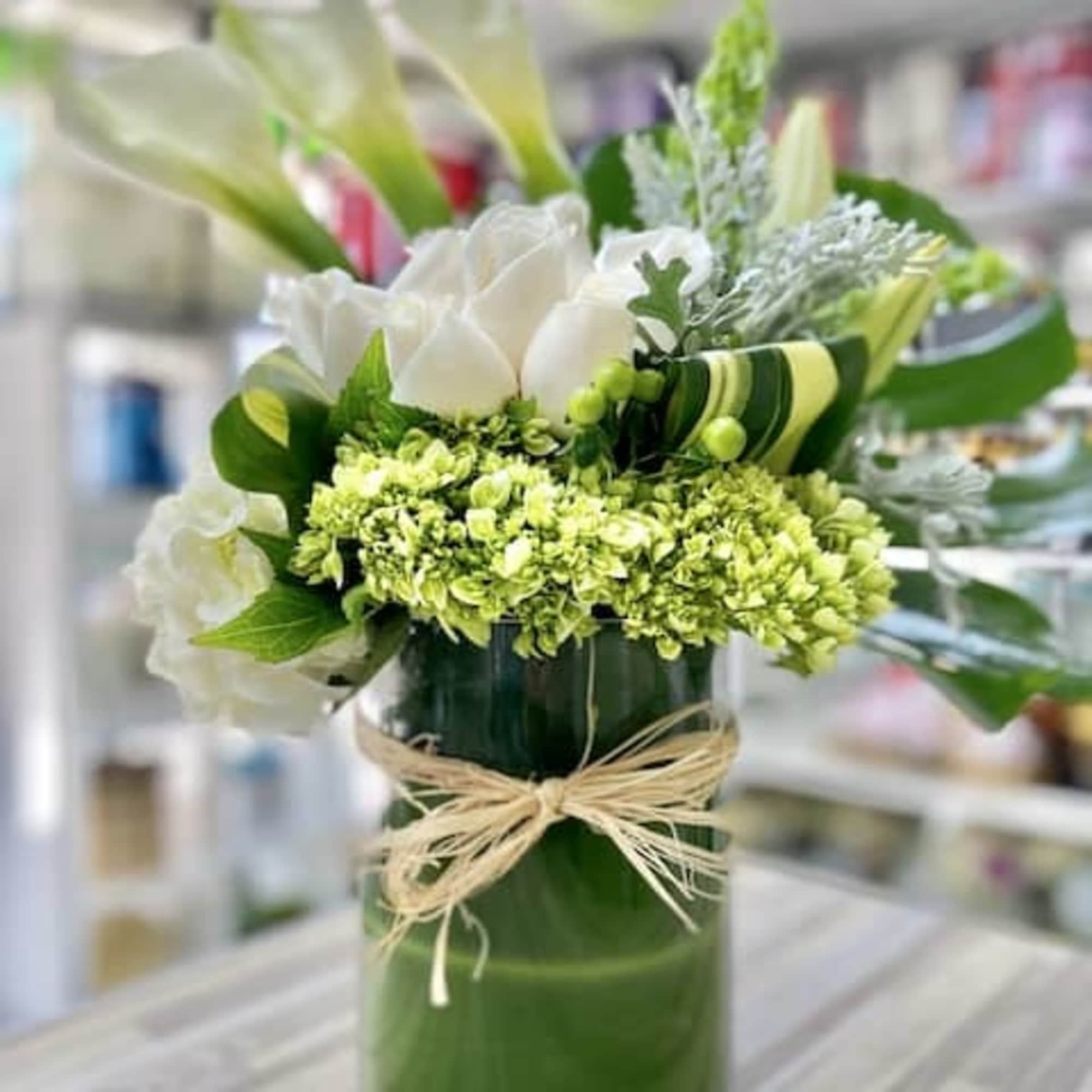 Tall glass vase of white calla lilies, roses, and green hydrangea tied with a raffia bow
