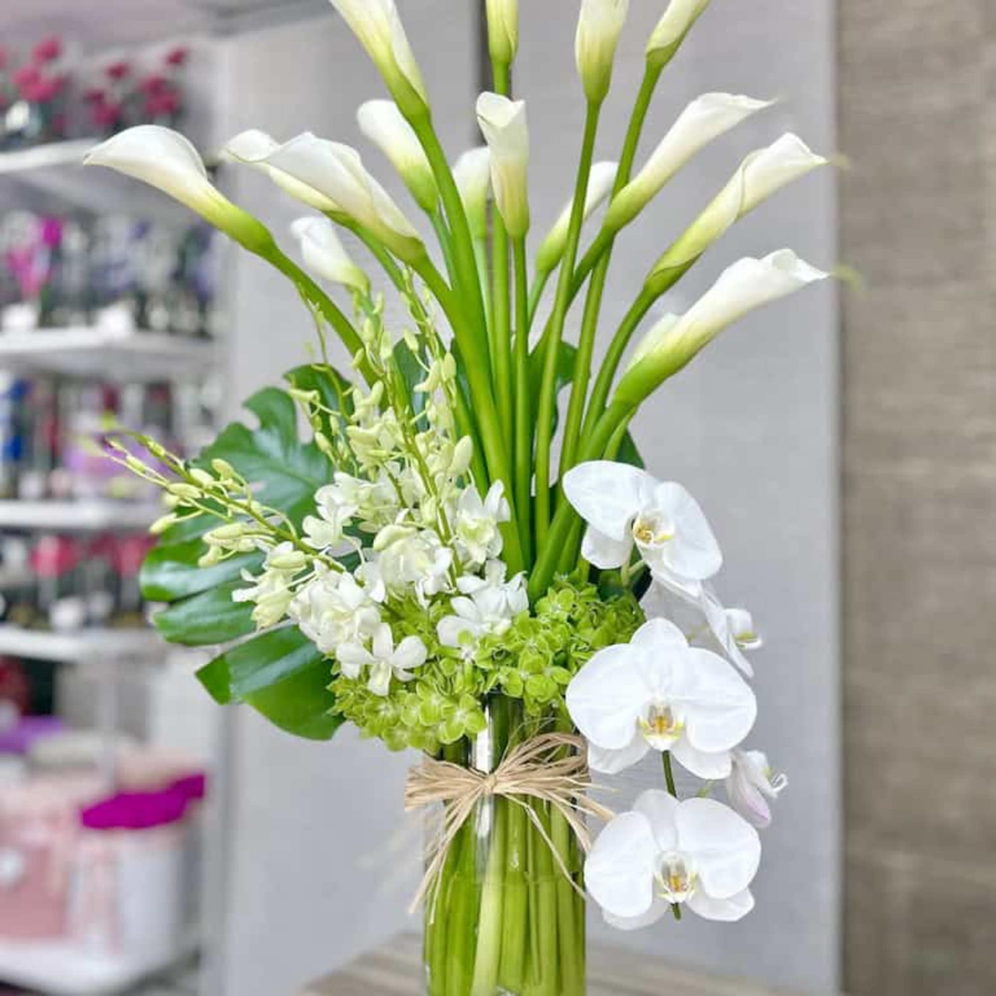 Tall arrangement of white calla lilies, orchids and green hydrangea in a clear glass vase