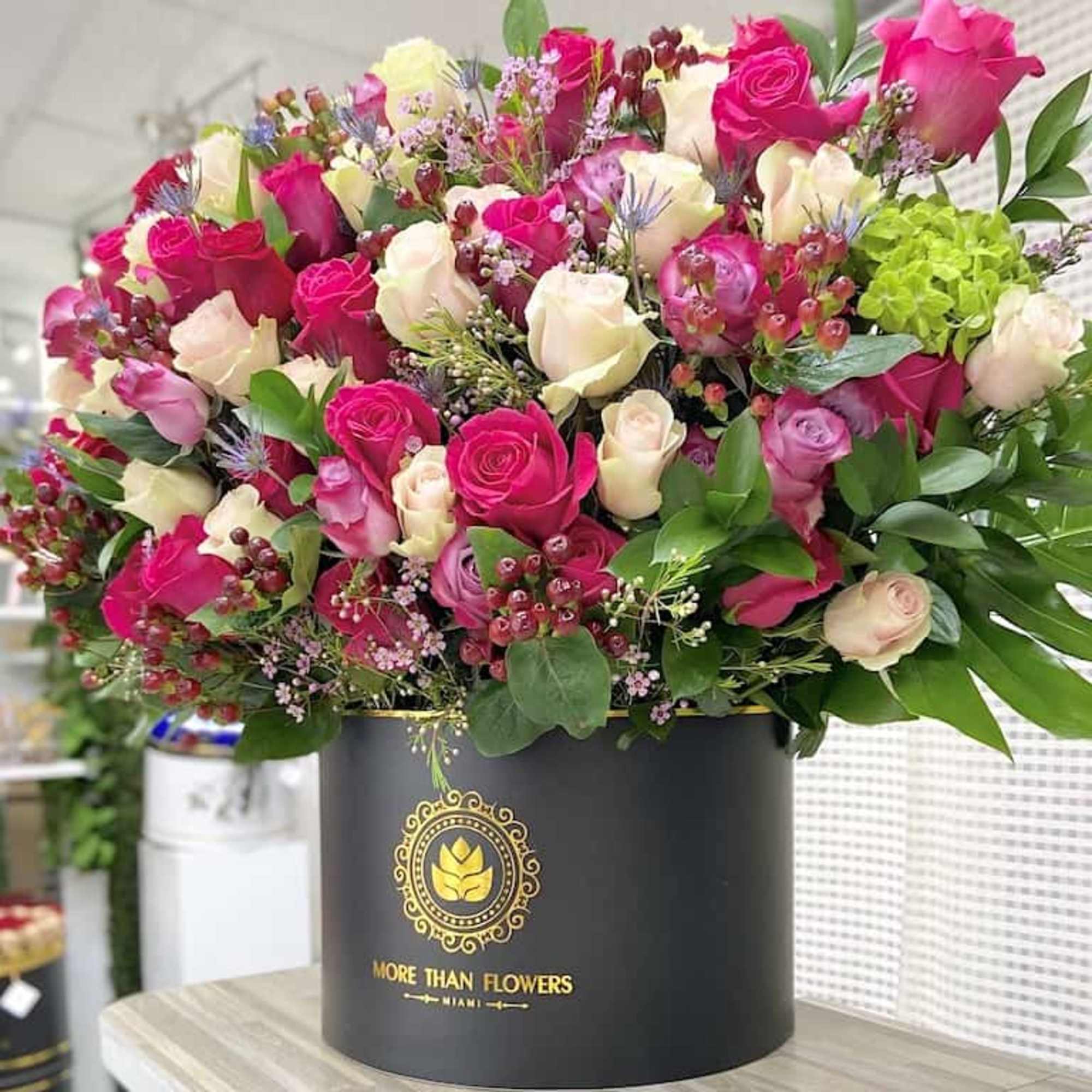 Large arrangement of hot pink and cream roses with accents in a black hat box container