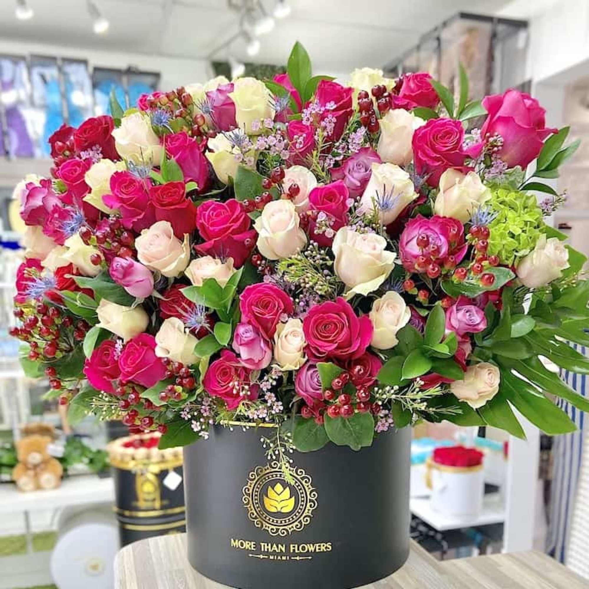Large arrangement of pink, red, and cream roses in a black hatbox-style container on a table